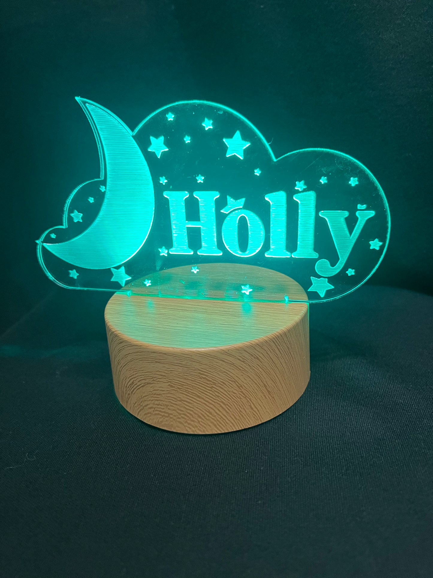 Custom acrylic LED night light with the name 'Holly' engraved in a cloud and moon design, glowing blue on a wooden-style base against a dark background