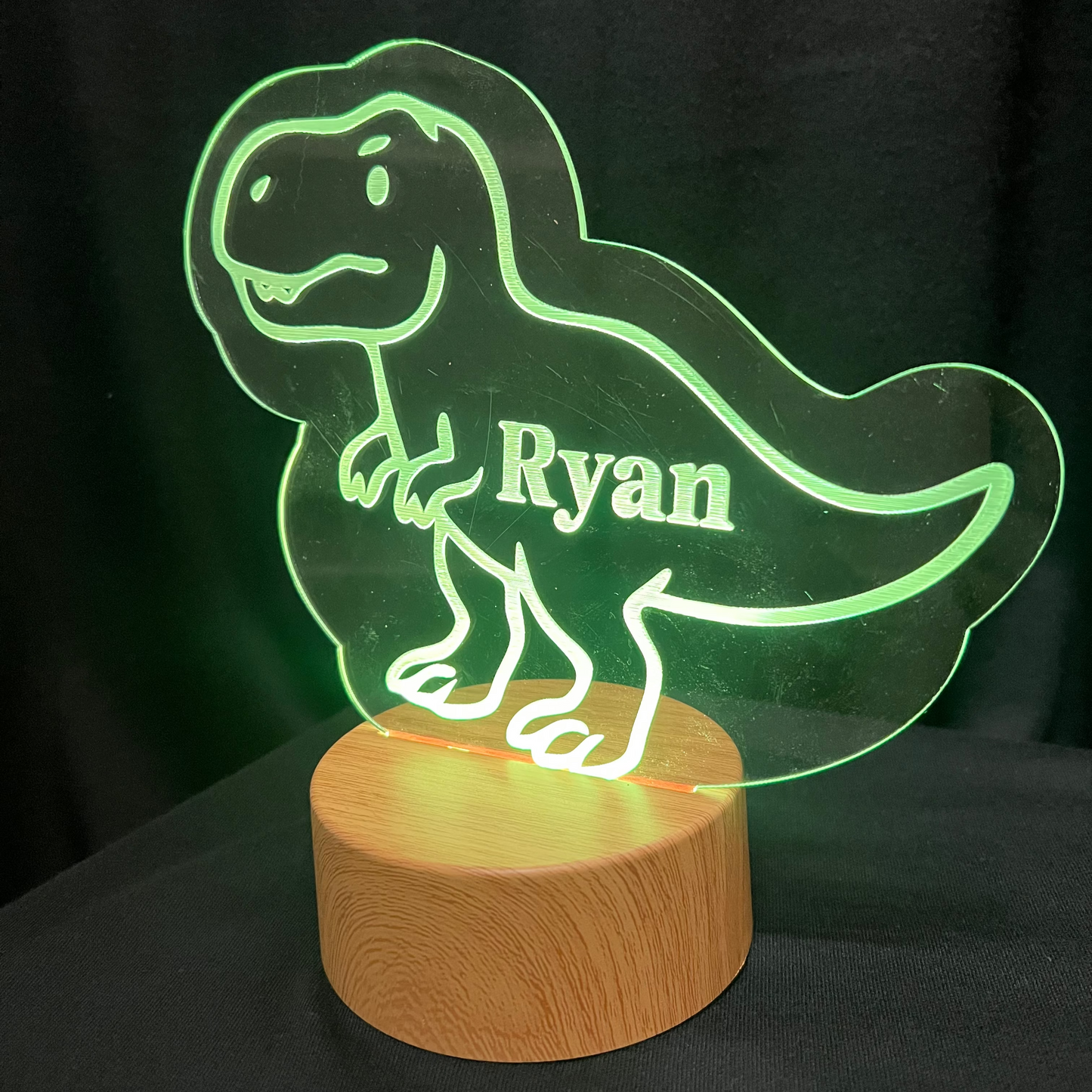 Dinosaur-shaped night light with 'Ryan' on a wooden base against a dark background