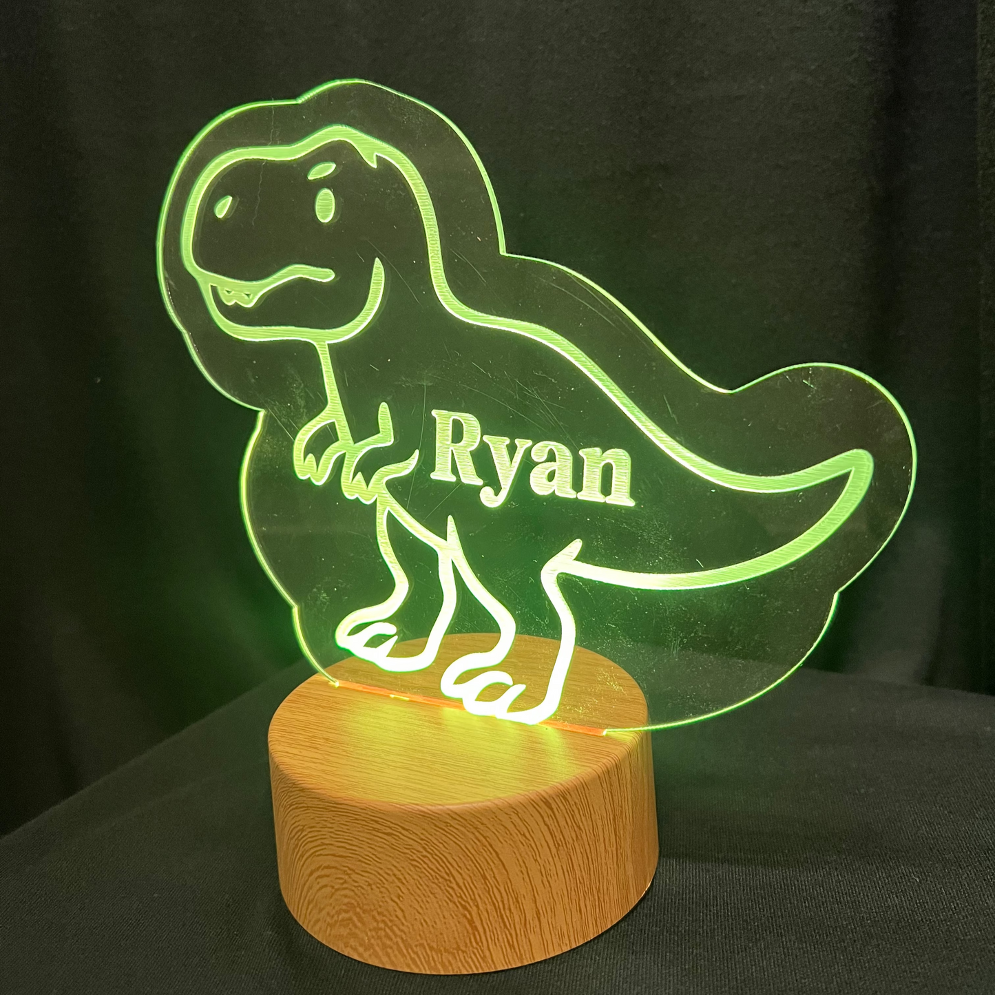 Dinosaur-shaped night light with 'Ryan' engraved on a wooden base against a dark background