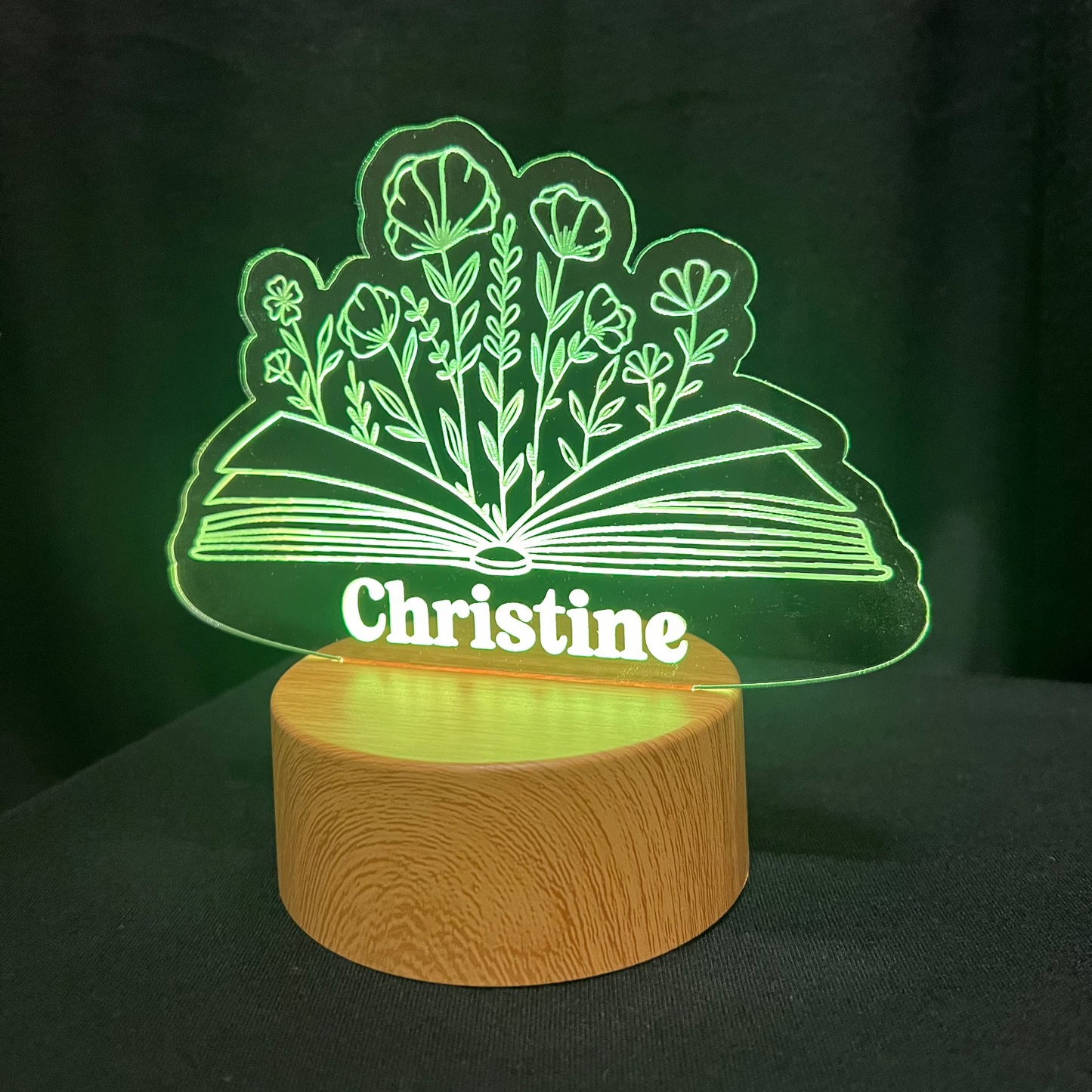 Decorative lamp with 'Christine' and a book with a floral design on a dark background