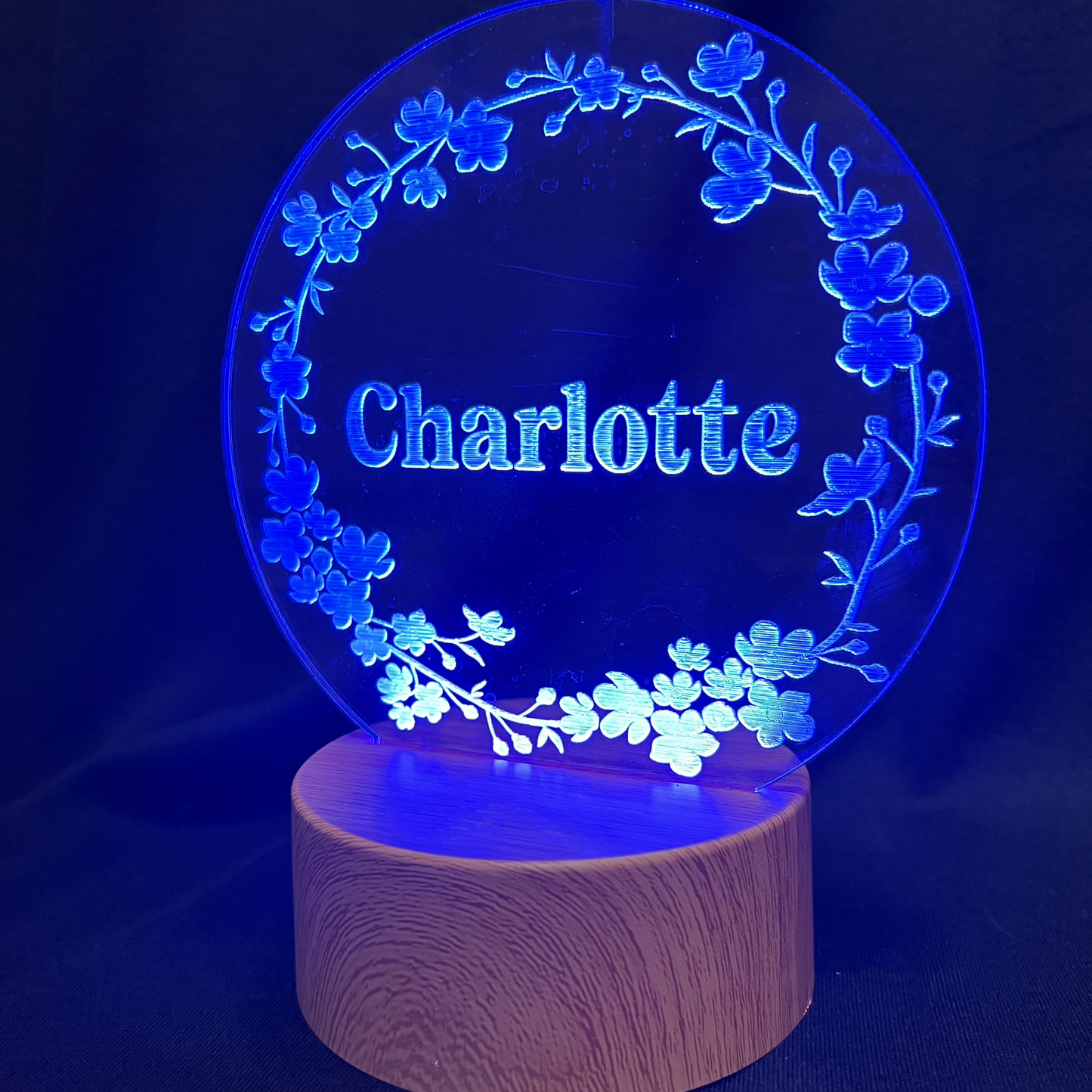 Personalized Floral Circle Night Light featuring a laser-engraved acrylic panel with a delicate floral wreath surrounding a custom name, illuminated by a warm LED light on a wooden base.
