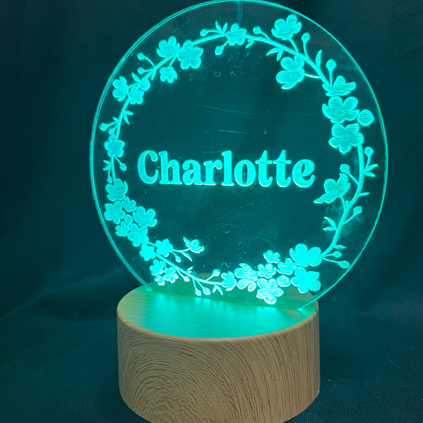 Personalized Floral Circle Night Light featuring a laser-engraved acrylic panel with a delicate floral wreath surrounding a custom name, illuminated by a warm LED light on a wooden base.
