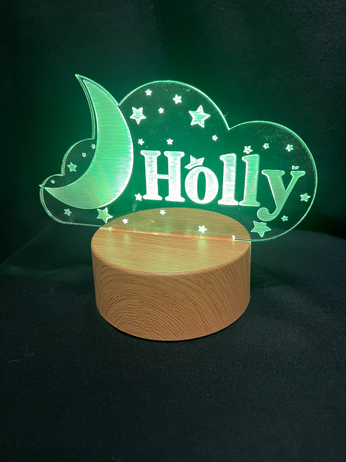 Custom acrylic LED night light with the name 'Holly' engraved in a cloud and moon design, glowing blue on a wooden-style base against a dark background