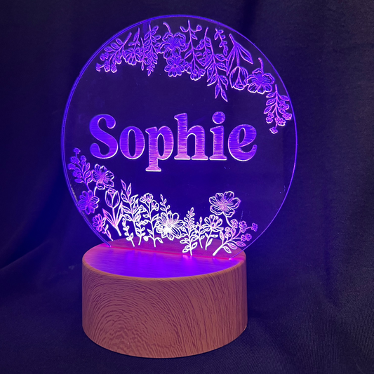 Personalized Wildflower Name Night Light featuring laser-engraved wildflowers surrounding a custom name on a clear acrylic panel, softly illuminated by an LED light on a wooden base