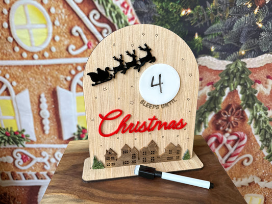Small wooden sign with a dry erase moon that says (blank) sleeps until Christmas with Santa's sleigh and a holiday village 