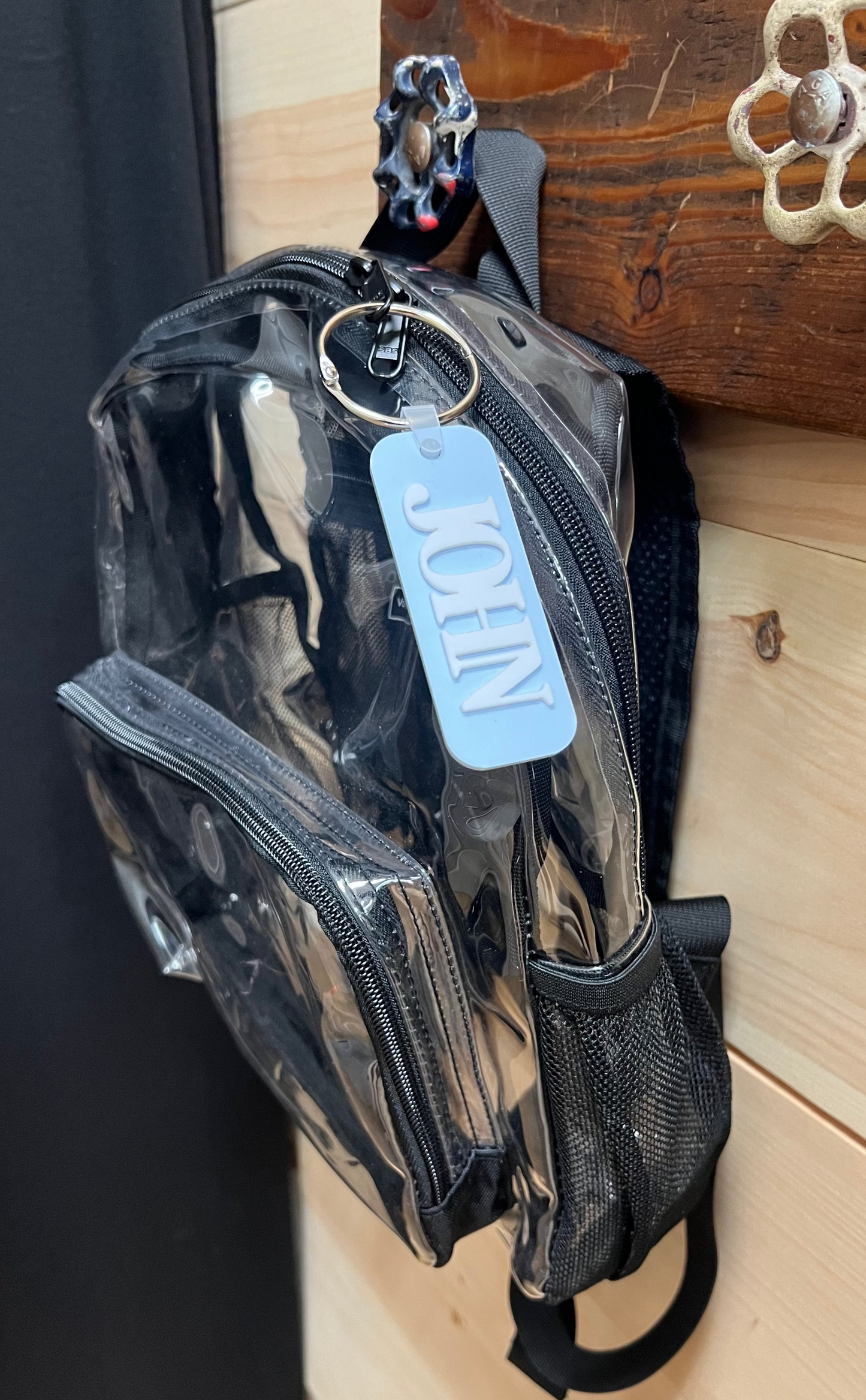 Clear pouch with black strap and blue tag on a wooden surface