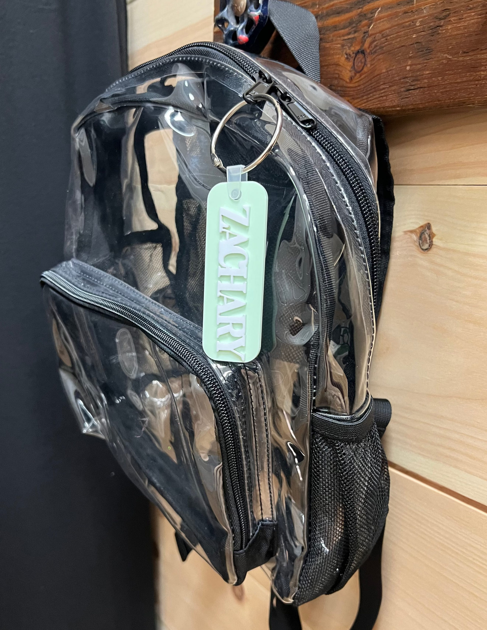 Clear backpack with a black strap hanging on a wooden surface