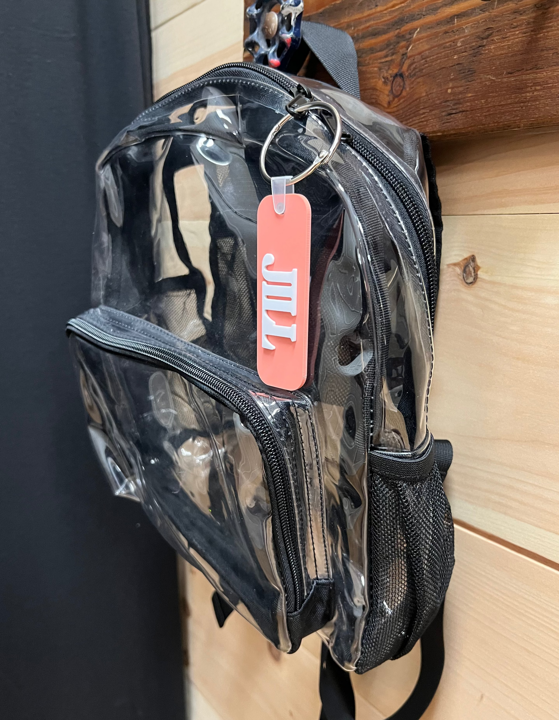 Clear backpack with a pink tag attached to a wooden surface