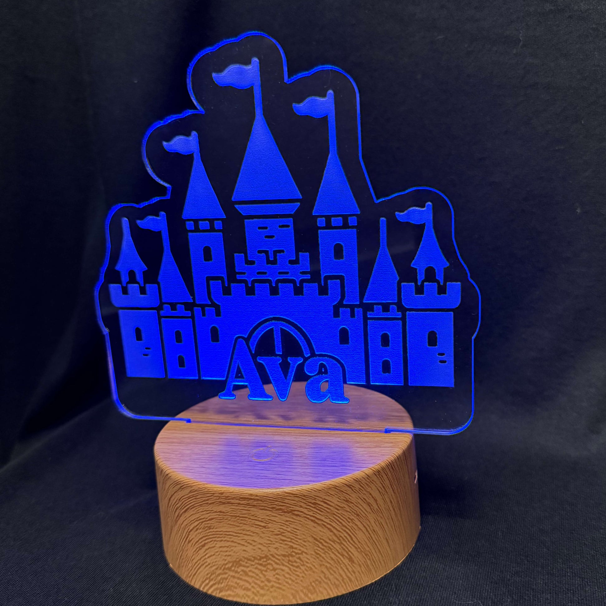 Blue castle-shaped night light on a wooden base against a black background