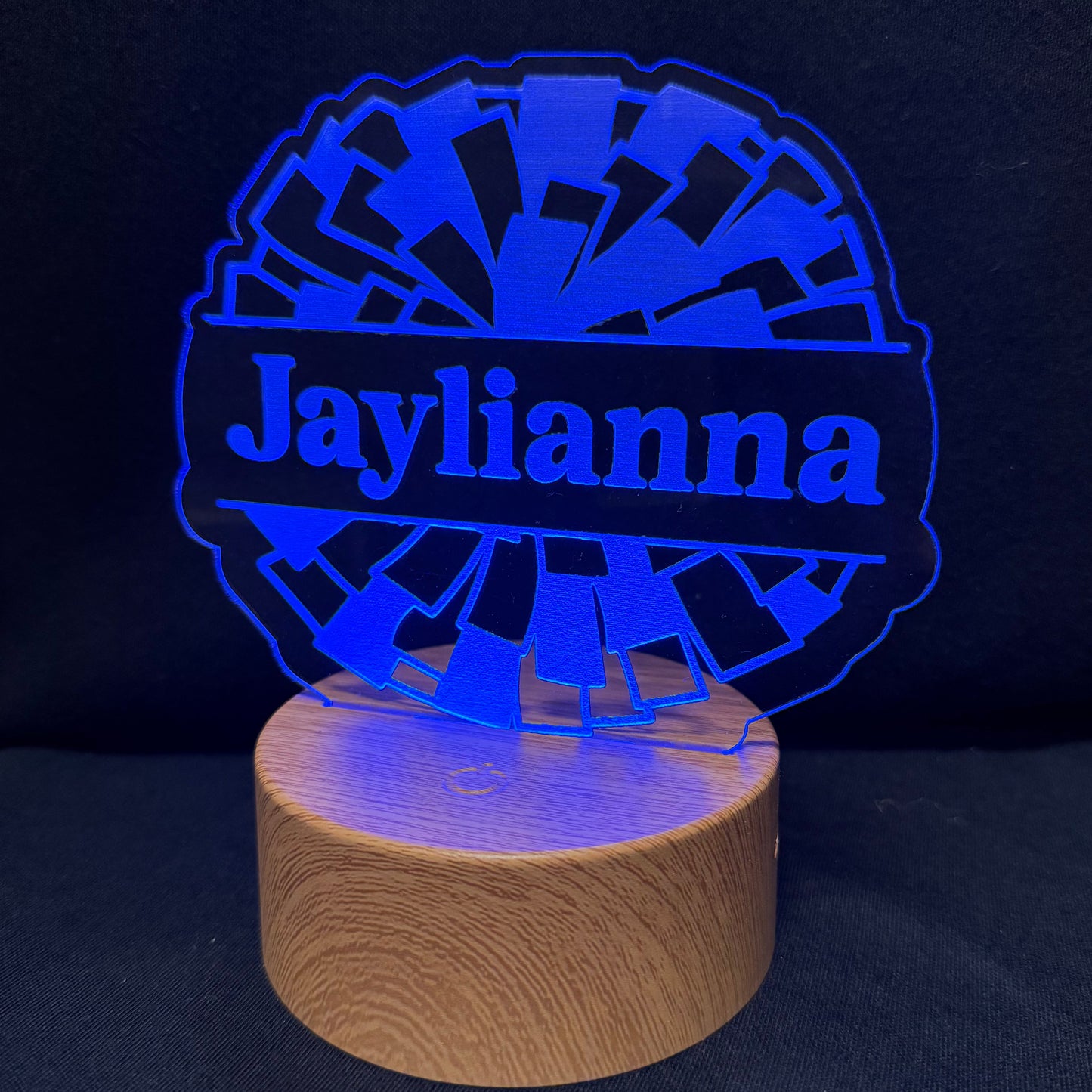 A personalized LED night light featuring a wooden cylindrical base and a blue laser-cut acrylic top with the name 'Jaylianna' in script, set against a dark background.