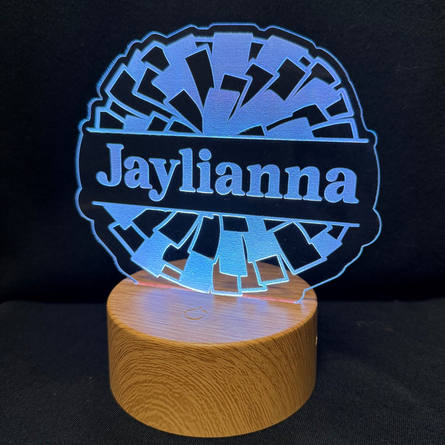 A personalized LED acrylic lamp with a circular blue light design spelling 'Jaylianna' on a cylindrical wooden base, set against a dark background.