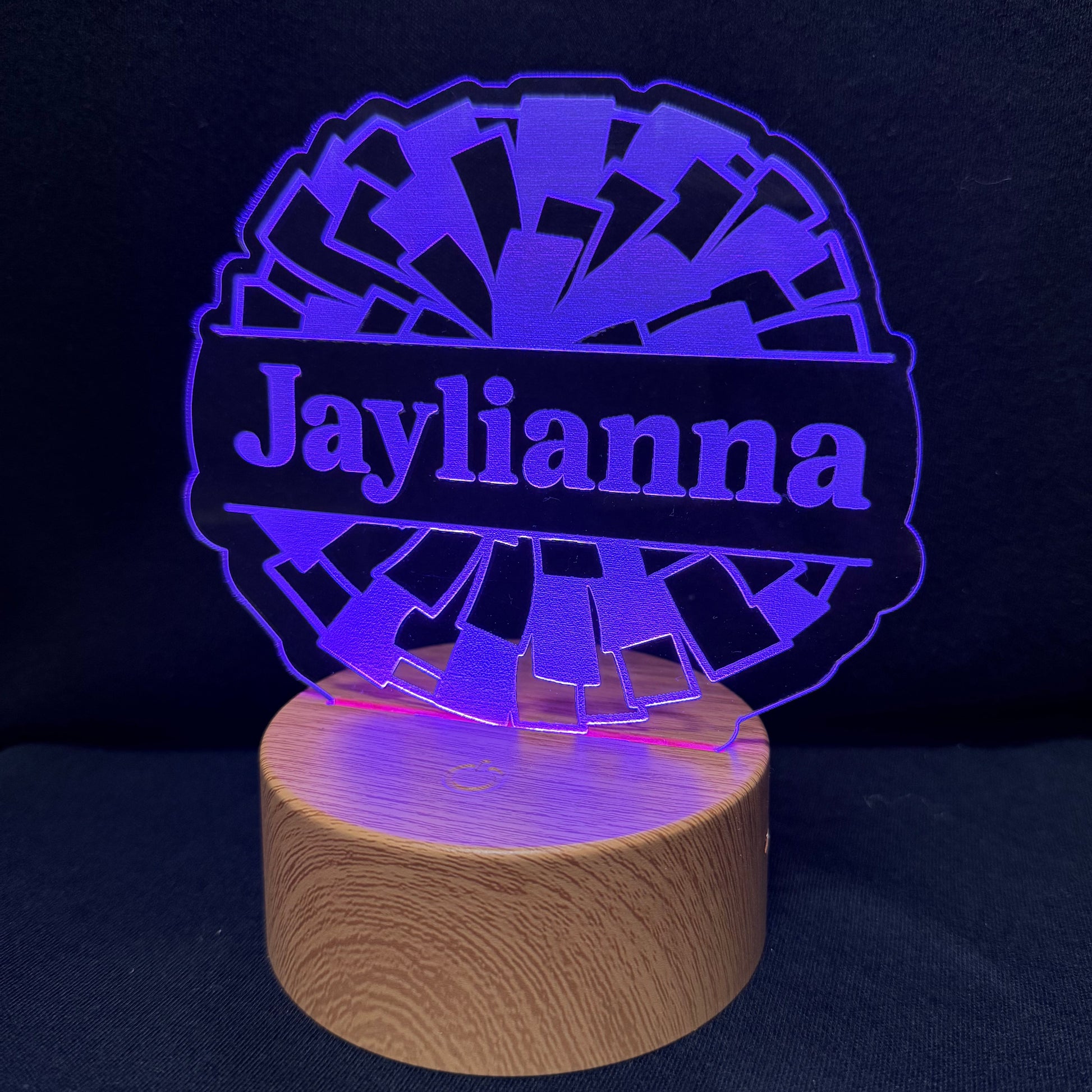 A personalized LED night light with a circular wooden base and a laser-cut acrylic top displaying the name 'Jaylianna' in purple, set against a dark background.