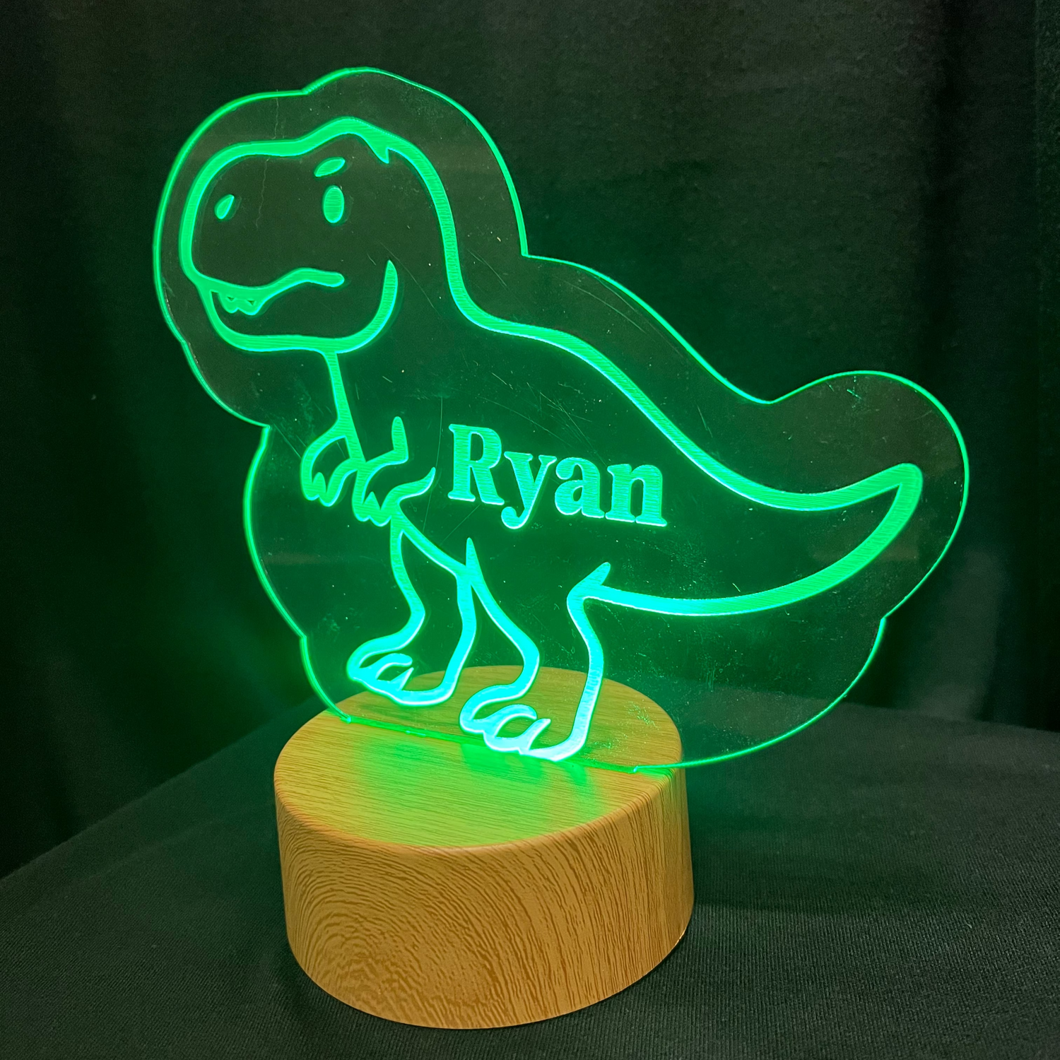 Dinosaur-shaped night light with 'Ryan' on a wooden base against a dark background
