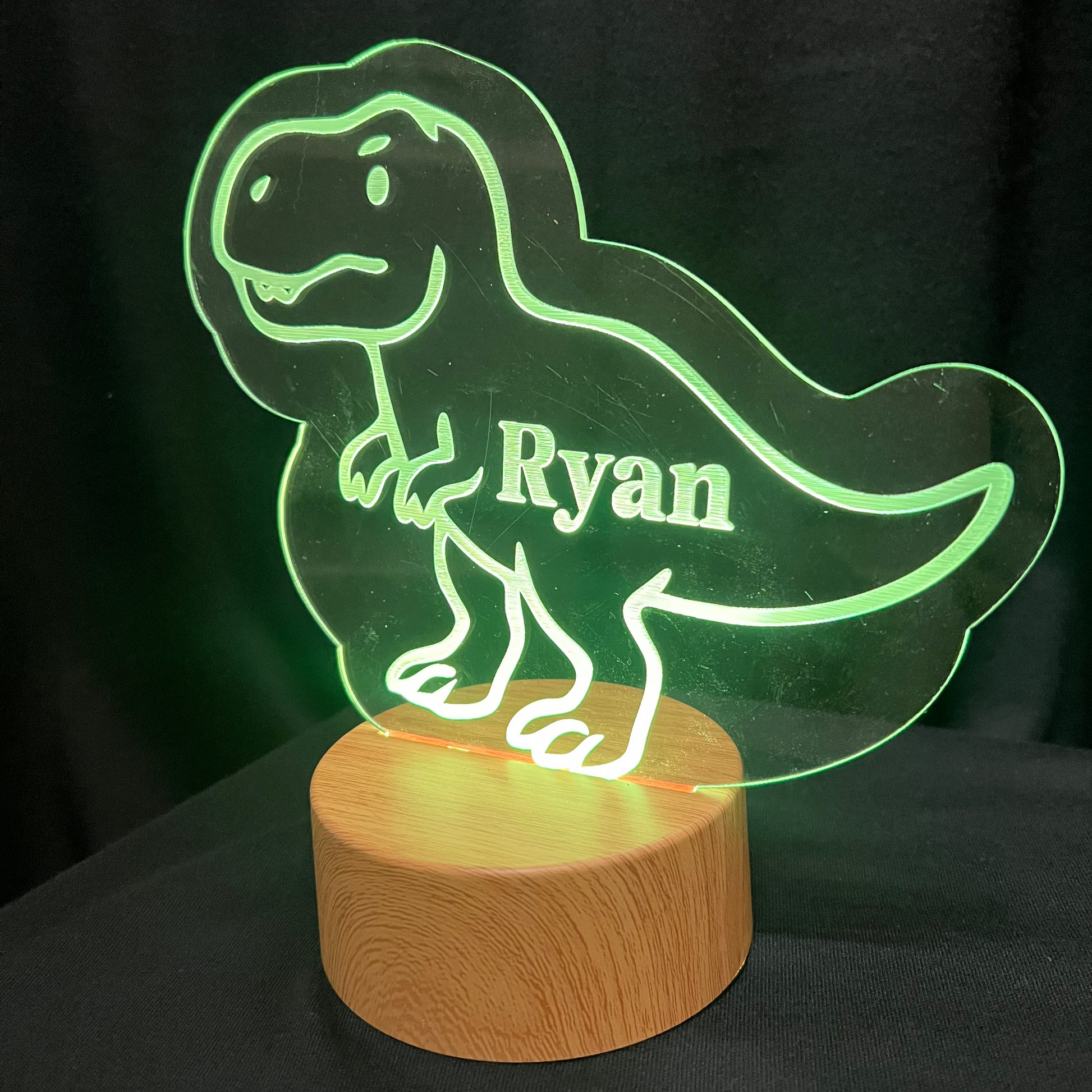 Dinosaur-shaped night light with 'Ryan' on a wooden base against a dark background