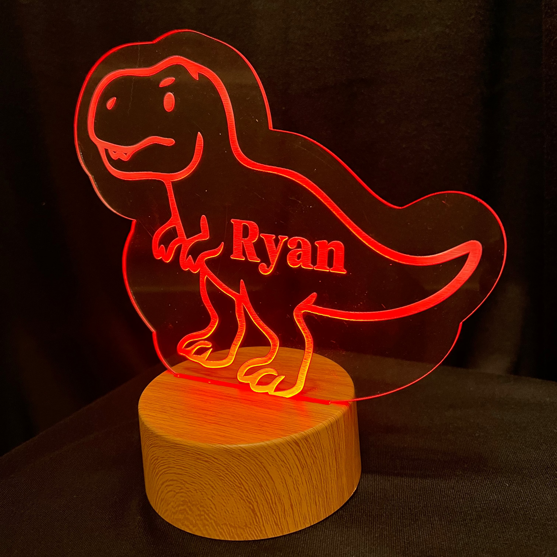 Dinosaur-shaped night light with 'Ryan' on a wooden base against a dark background