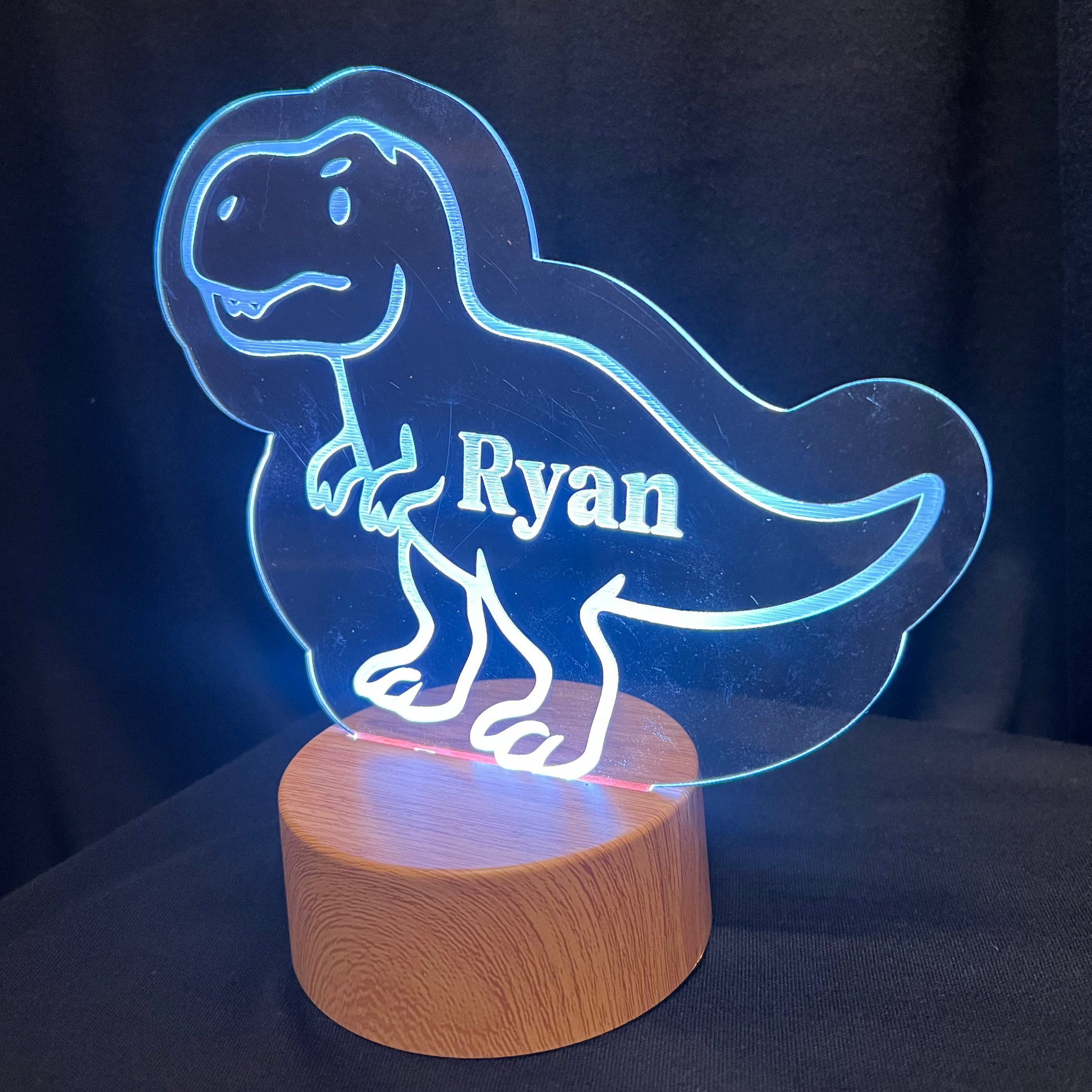 Dinosaur-shaped LED lamp with 'Ryan' on a wooden base against a dark background
