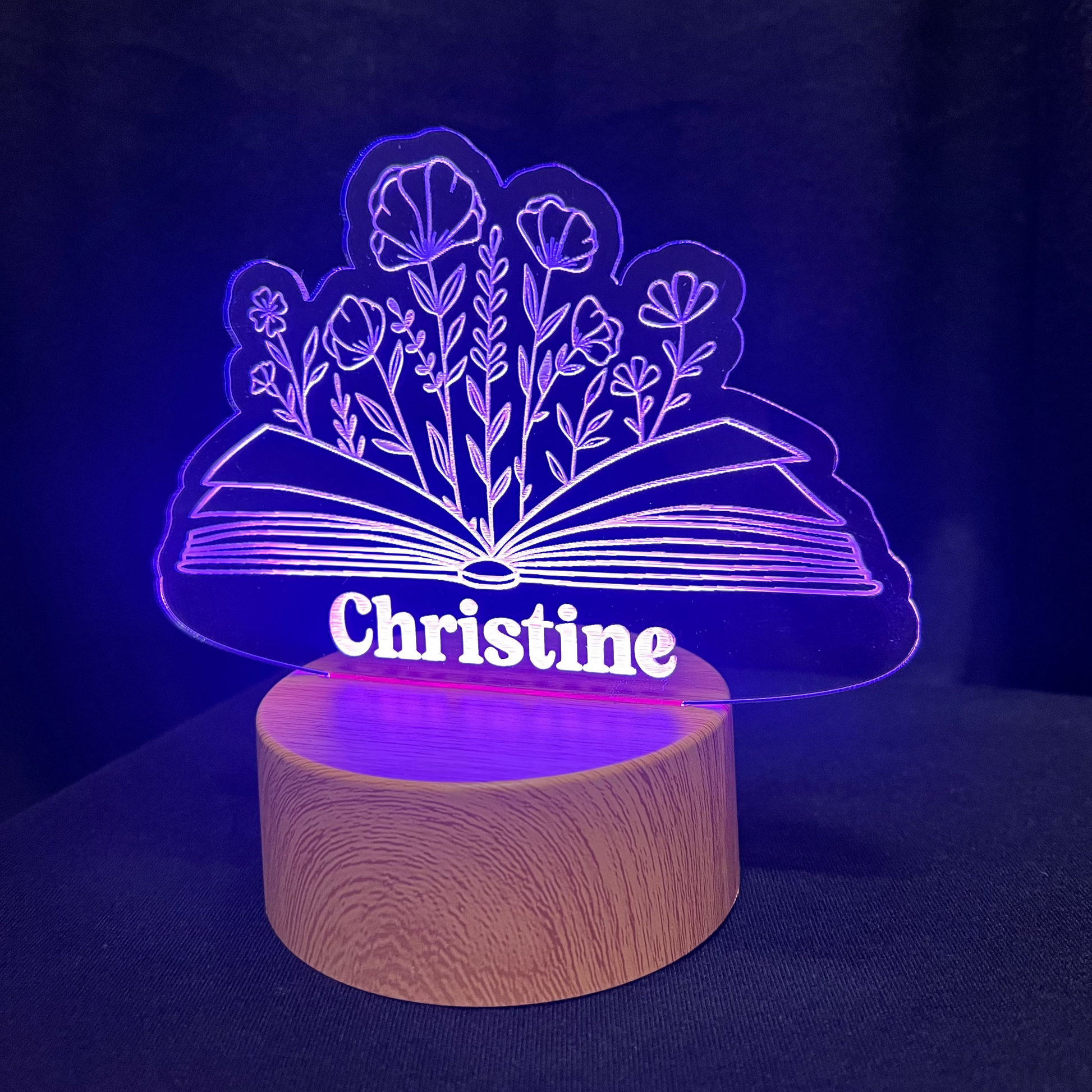 LED lamp with 'Christine' and a floral book design on a wooden base against a dark background