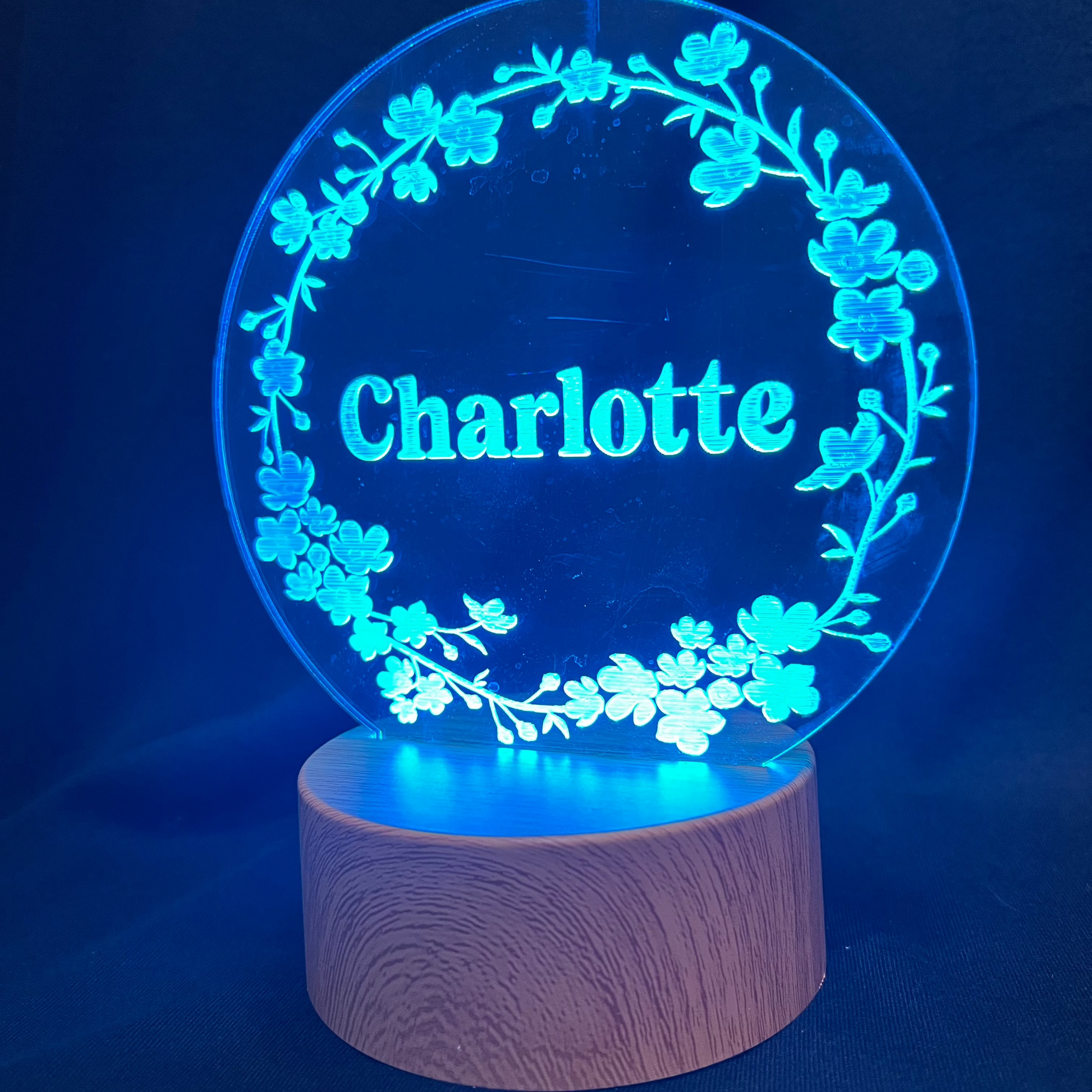 Personalized Floral Circle Night Light featuring a laser-engraved acrylic panel with a delicate floral wreath surrounding a custom name, illuminated by a warm LED light on a wooden base.