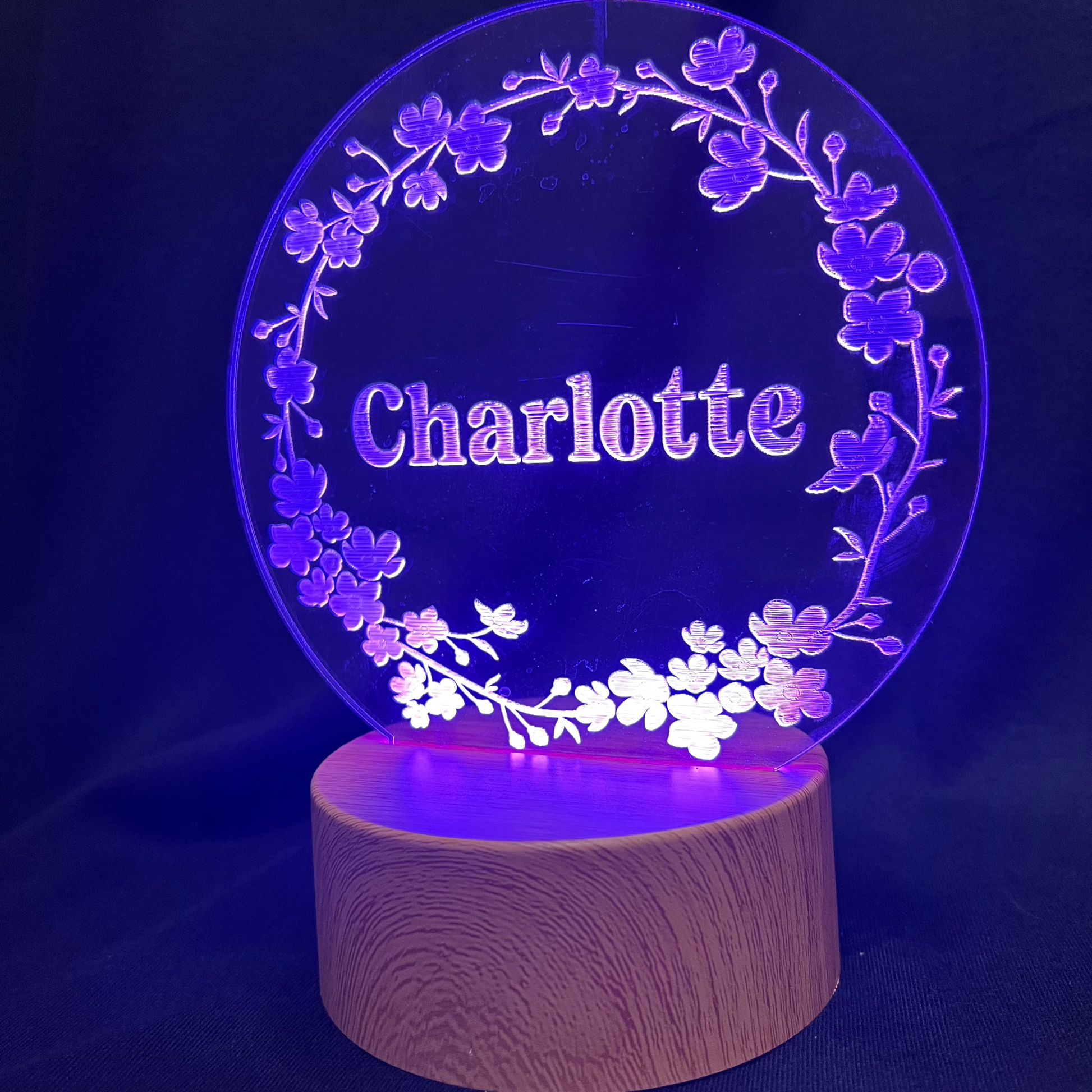 Personalized Floral Circle Night Light featuring a laser-engraved acrylic panel with a delicate floral wreath surrounding a custom name, illuminated by a warm LED light on a wooden base.