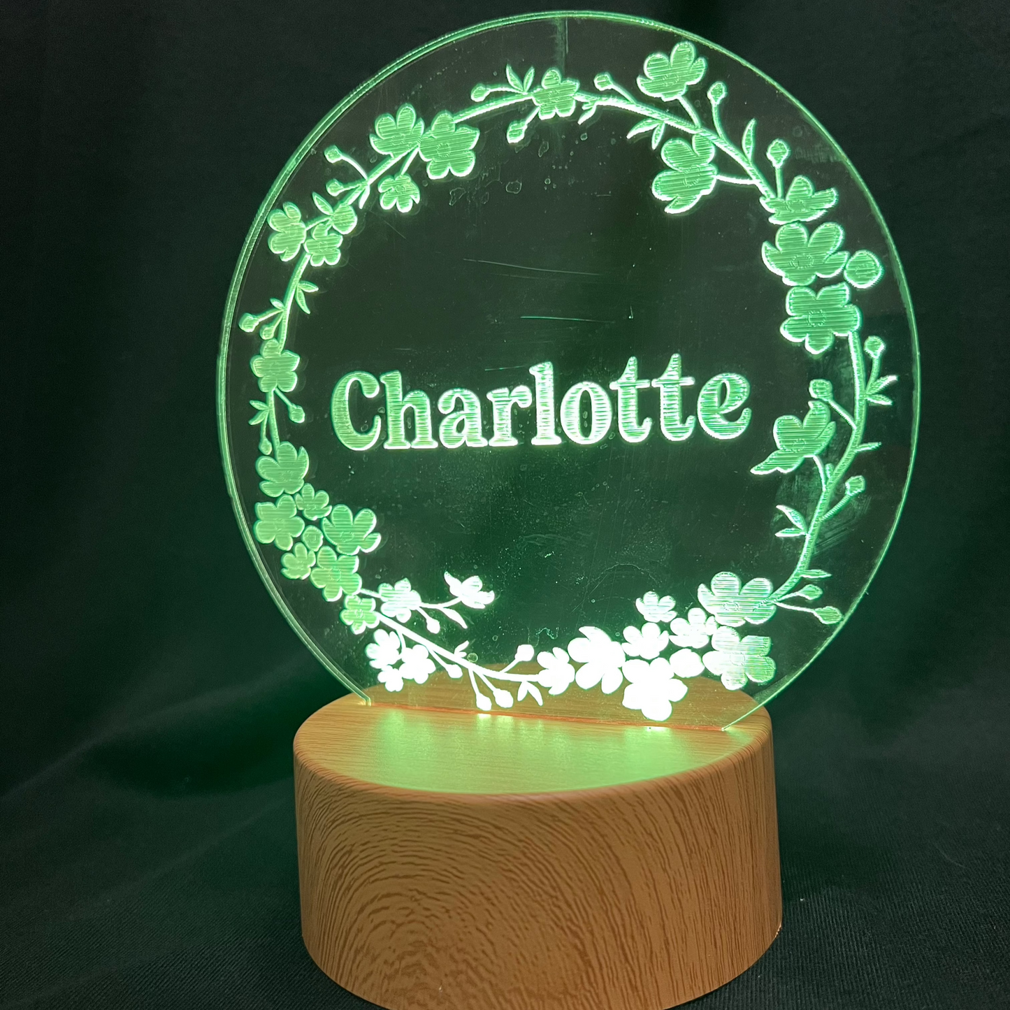 Personalized Floral Circle Night Light featuring a laser-engraved acrylic panel with a delicate floral wreath surrounding a custom name, illuminated by a warm LED light on a wooden base.