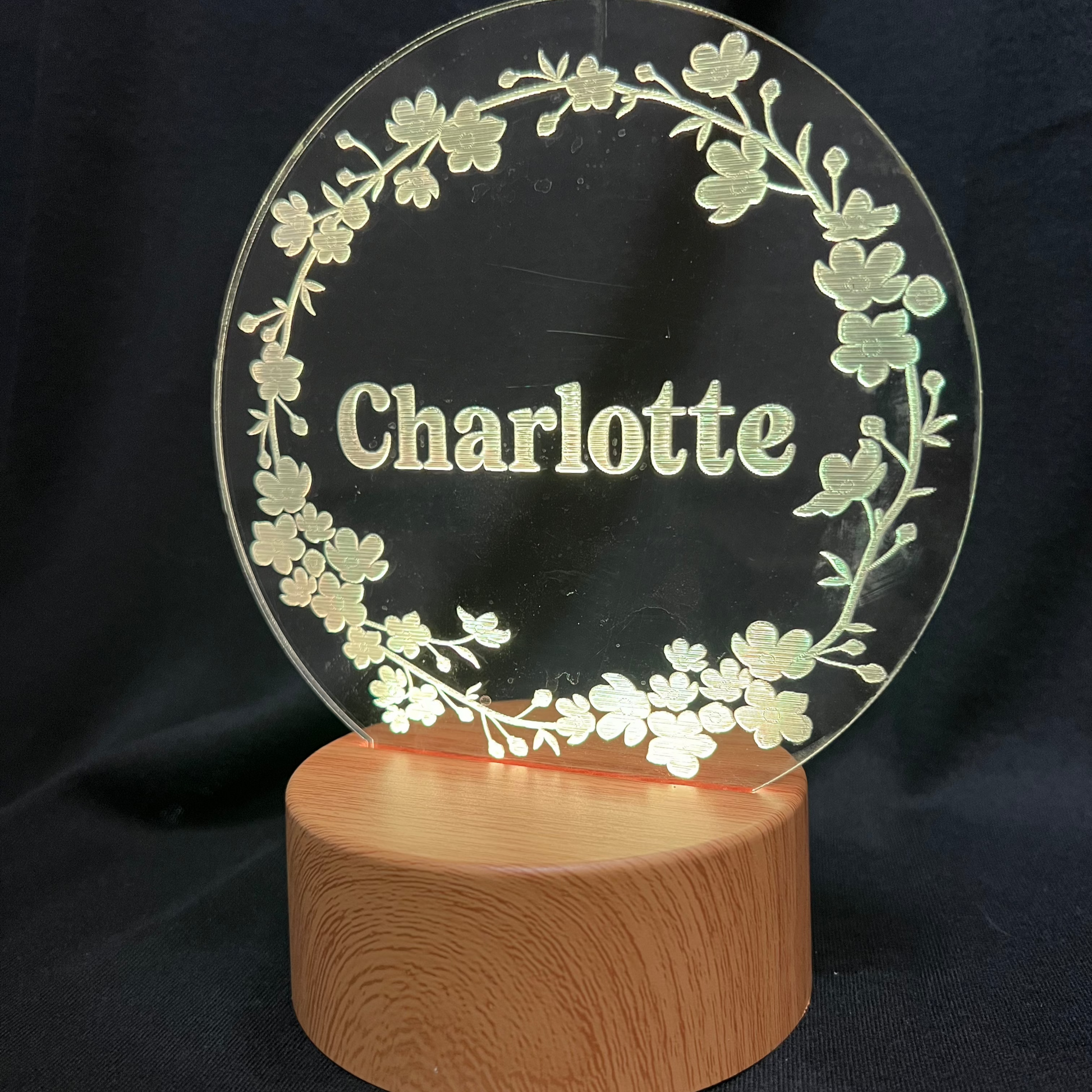Personalized Floral Circle Night Light featuring a laser-engraved acrylic panel with a delicate floral wreath surrounding a custom name, illuminated by a warm LED light on a wooden base.
