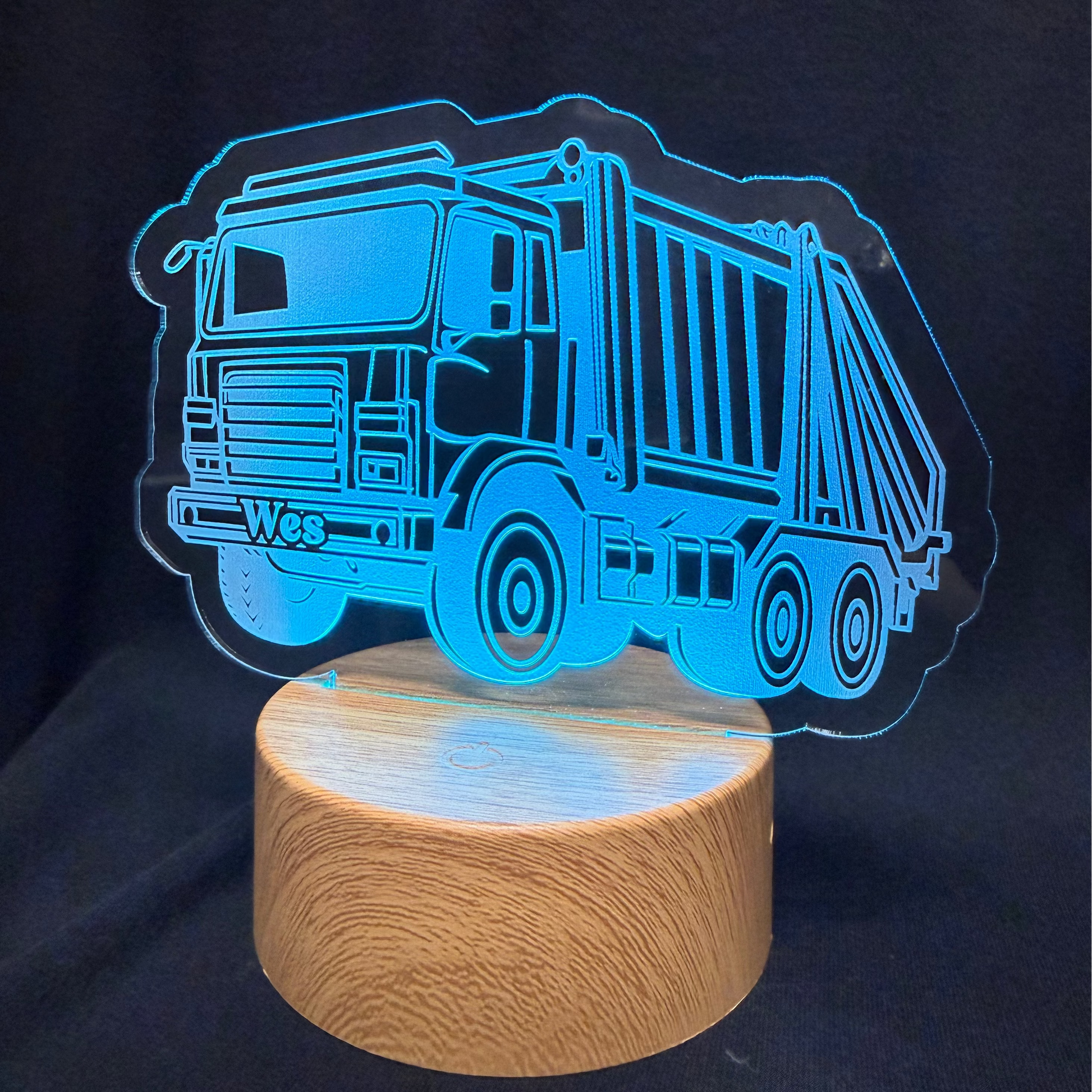 Blue truck-shaped night light on a wooden base against a black background