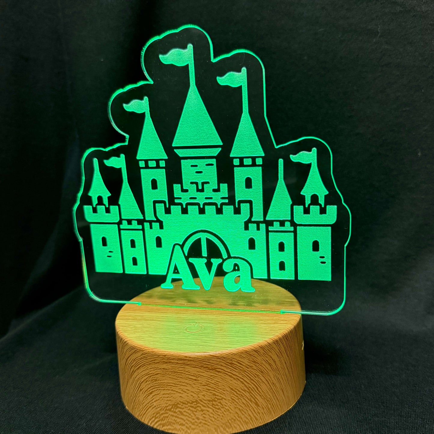 Glowing green castle-shaped night light on a wooden base against a black background