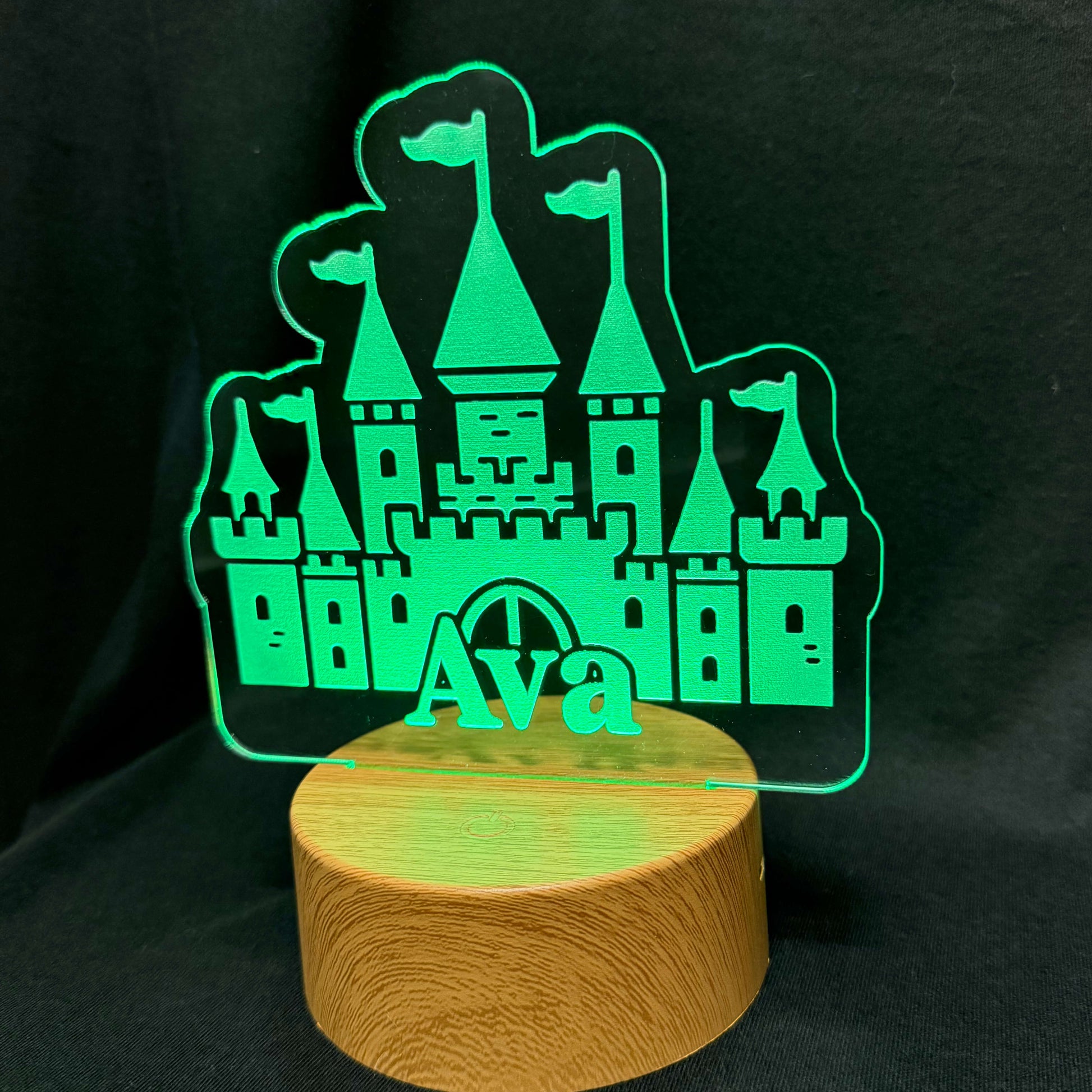 Glowing green castle-shaped night light on a wooden base against a black background