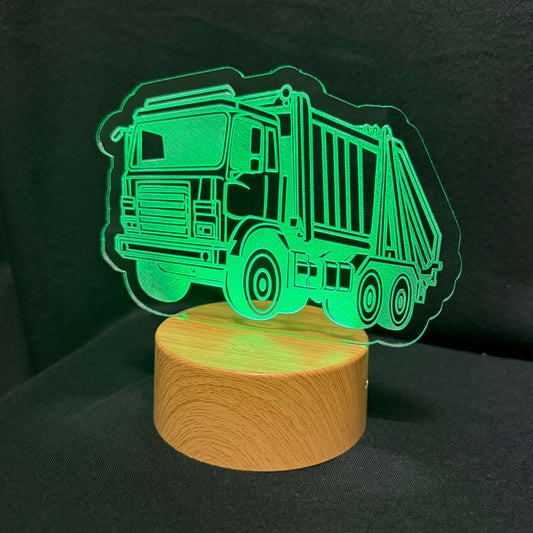 A truck-shaped LED night light with a glowing green laser-cut acrylic design mounted on a round wooden base, photographed against a dark background.