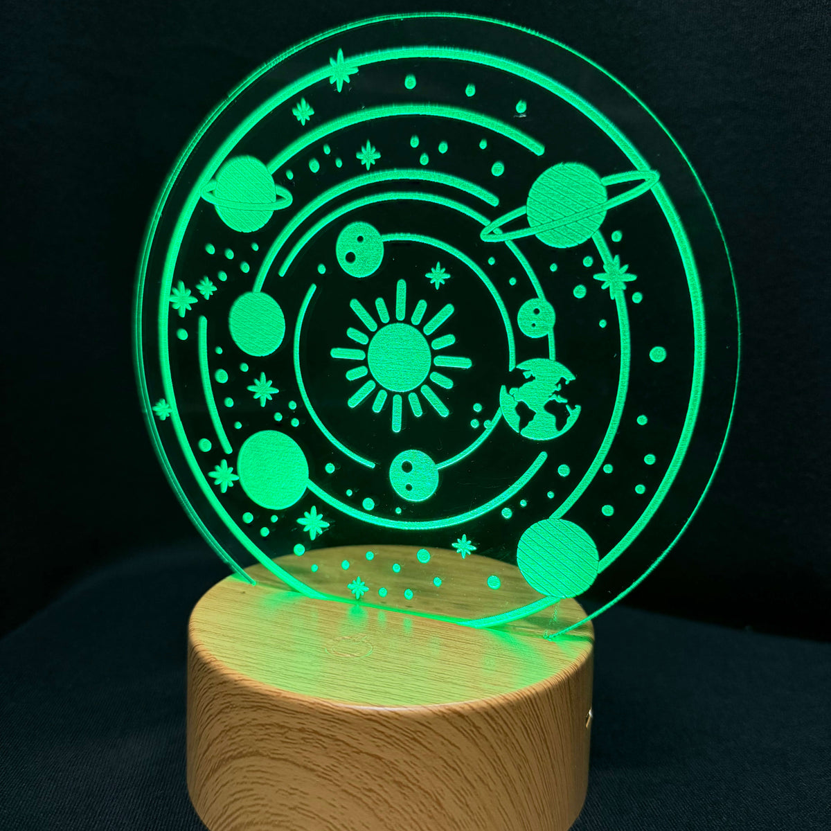An LED acrylic night light featuring a glowing green solar system design on a round wooden base, set against a dark background.