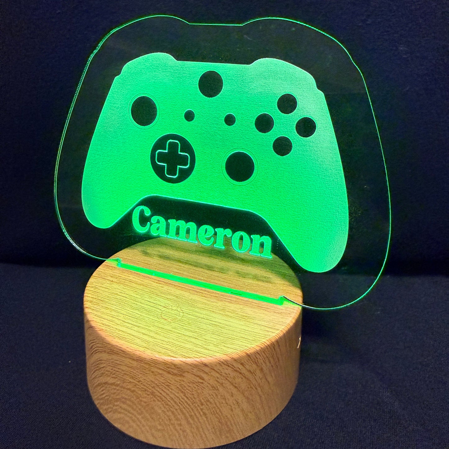 A personalized gaming-themed LED light featuring a glowing green controller silhouette with the name 'Cameron' on a round wooden base, set against a dark background.
