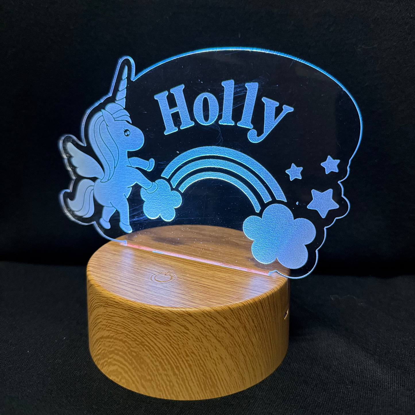 Decorative night light with unicorn, rainbow, and stars design on a wooden base against a black background.