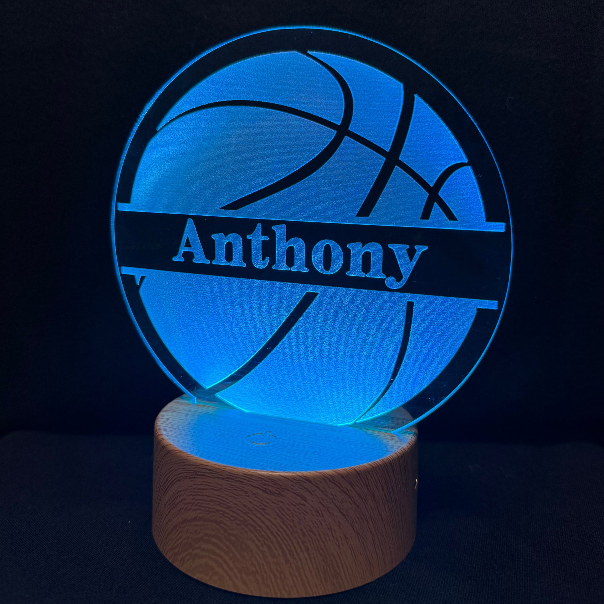 A personalized 3D optical illusion LED night light shaped like a basketball, featuring the name 'Anthony' illuminated in blue on a wooden base against a dark background.