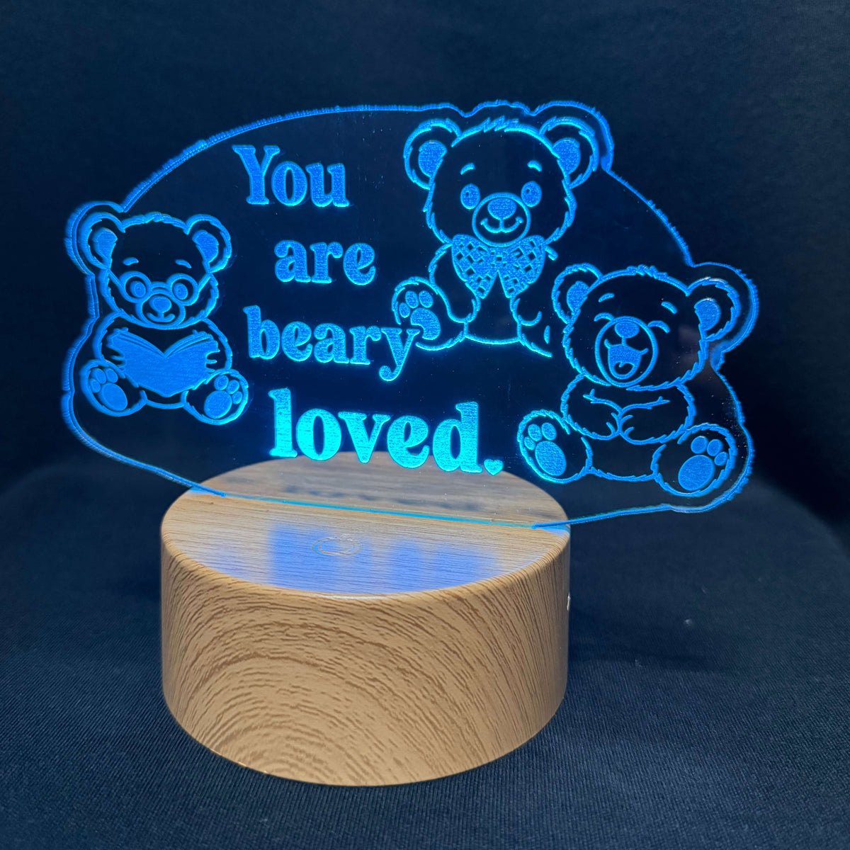 A wooden LED night light with a glowing blue acrylic panel featuring three teddy bears and the text 'You are beary loved.' on a dark navy background.