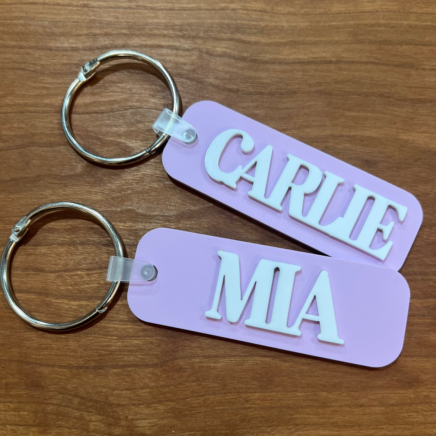 Two purple keychains with 'CARLIE' and 'MIA' engraved on a wooden surface