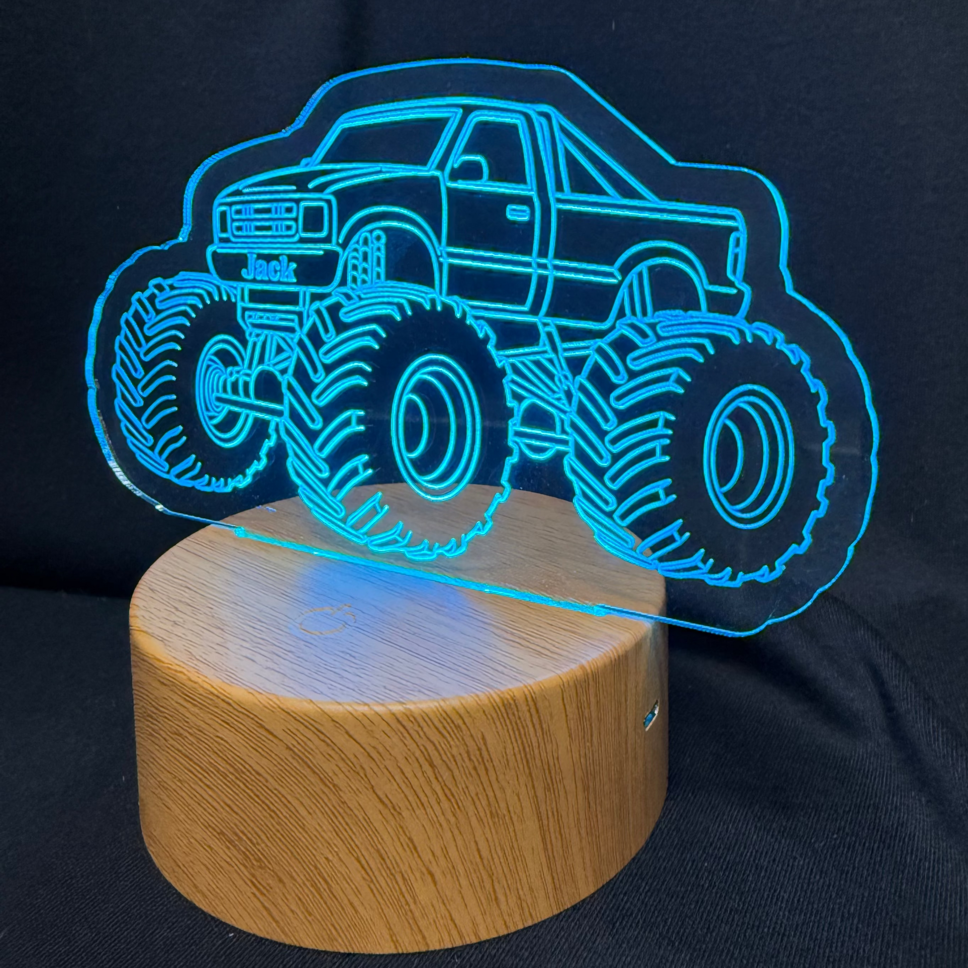 Monster truck night light on a wooden base with blue LED illumination against a dark background