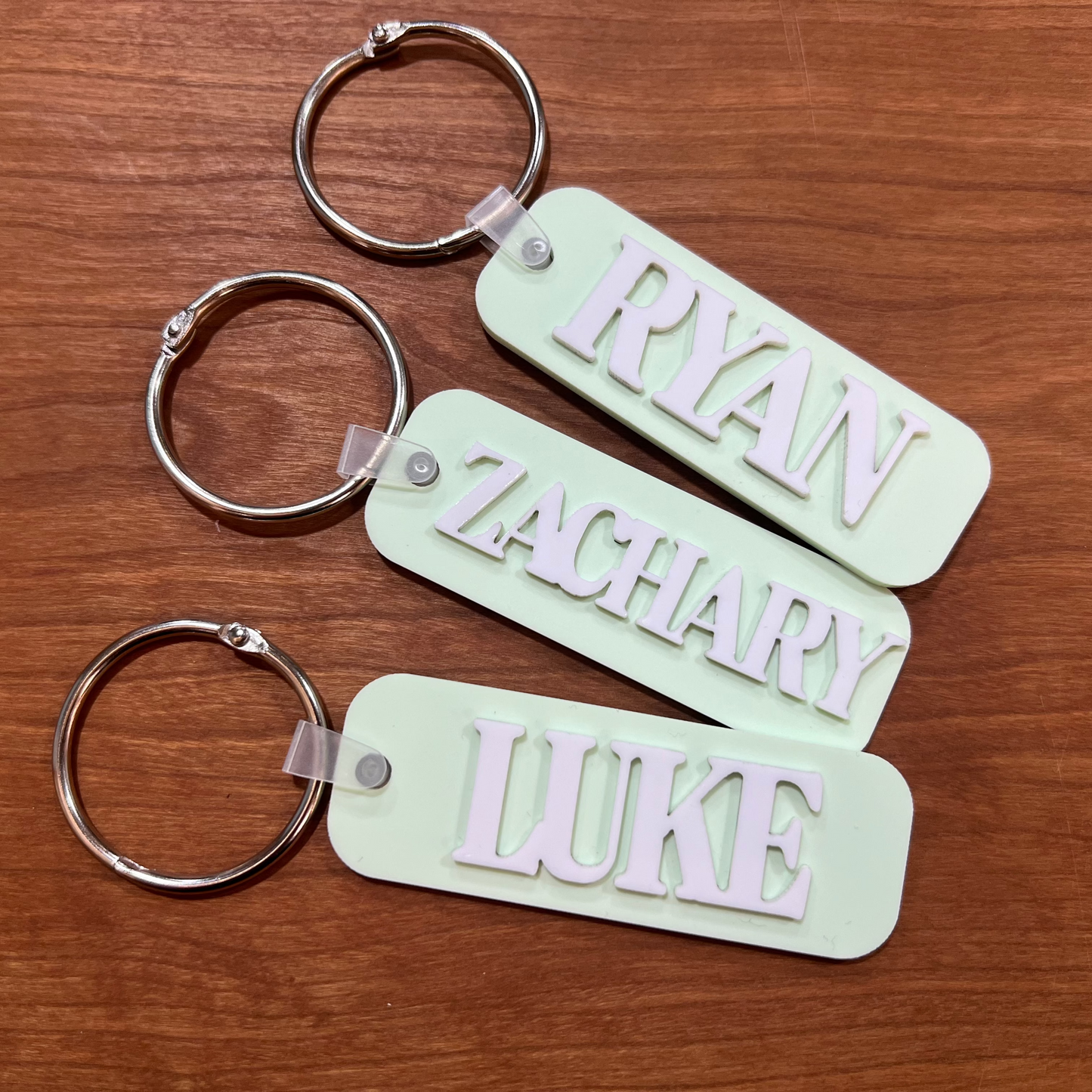 Three pastel green bag tags with names on them