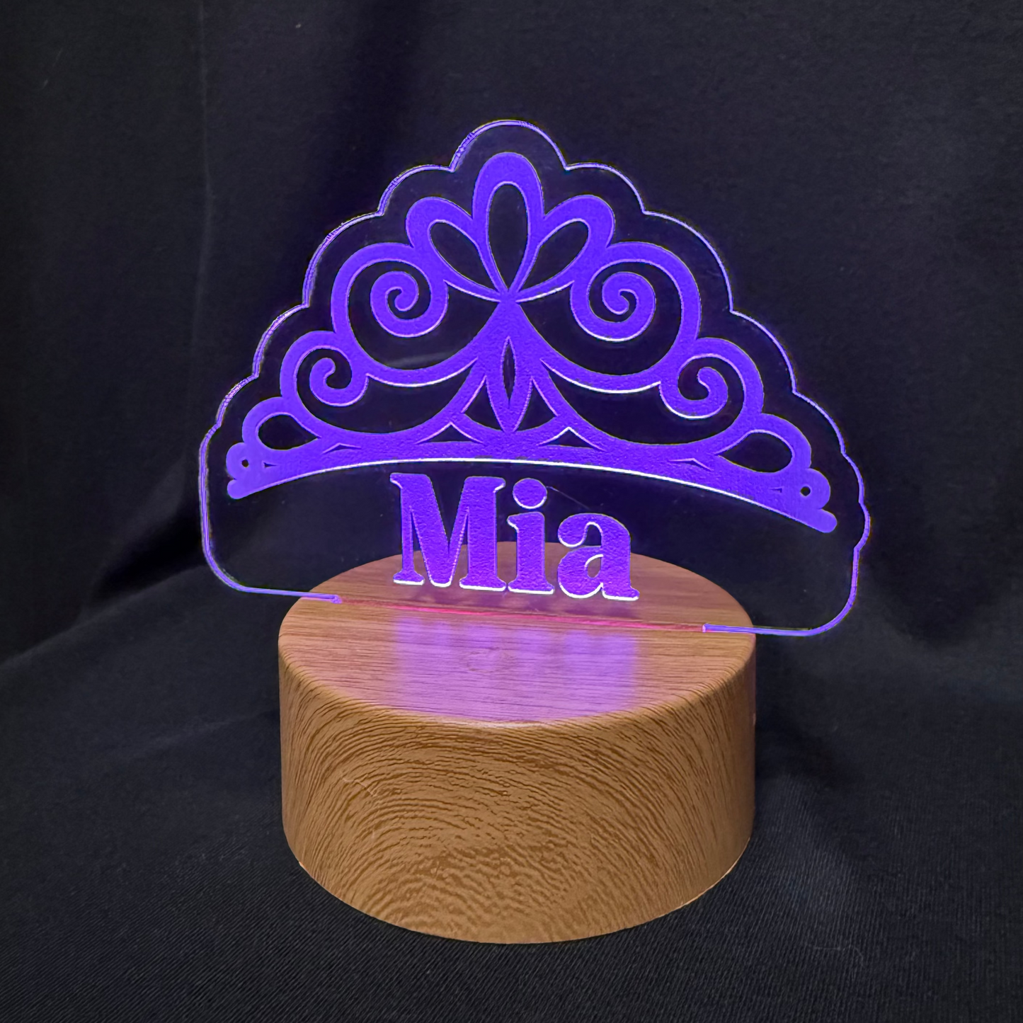 Acrylic tiara-shaped night light with 'Mia' on a wooden base against a black background