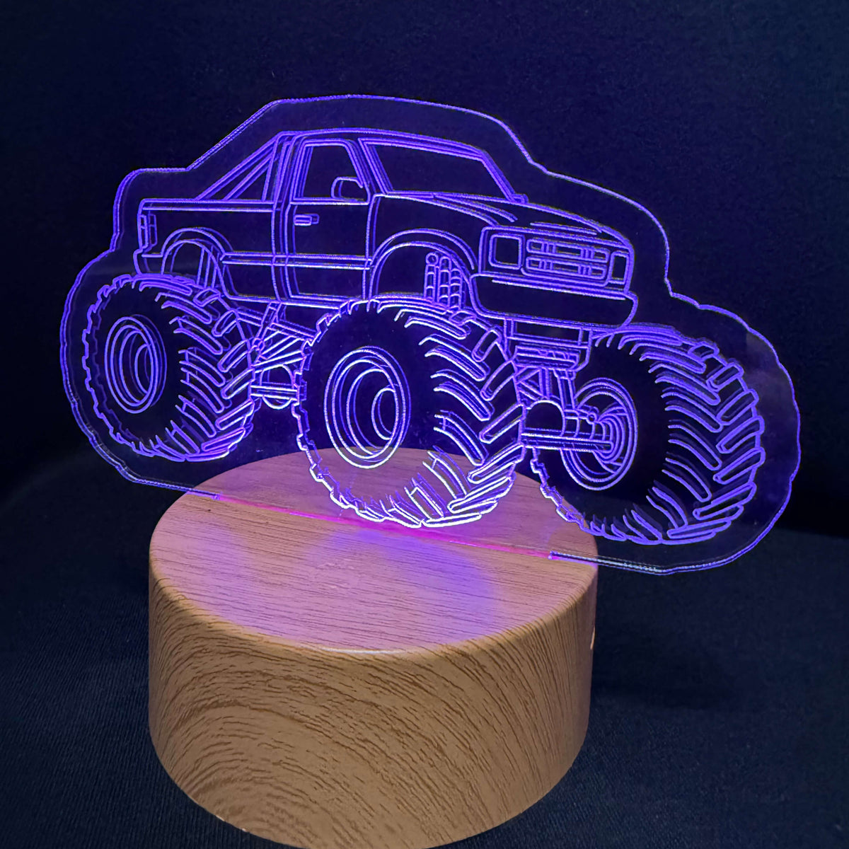 An LED acrylic lamp featuring a glowing purple outline of a monster truck on a round, light wood-grain base, set against a dark background.