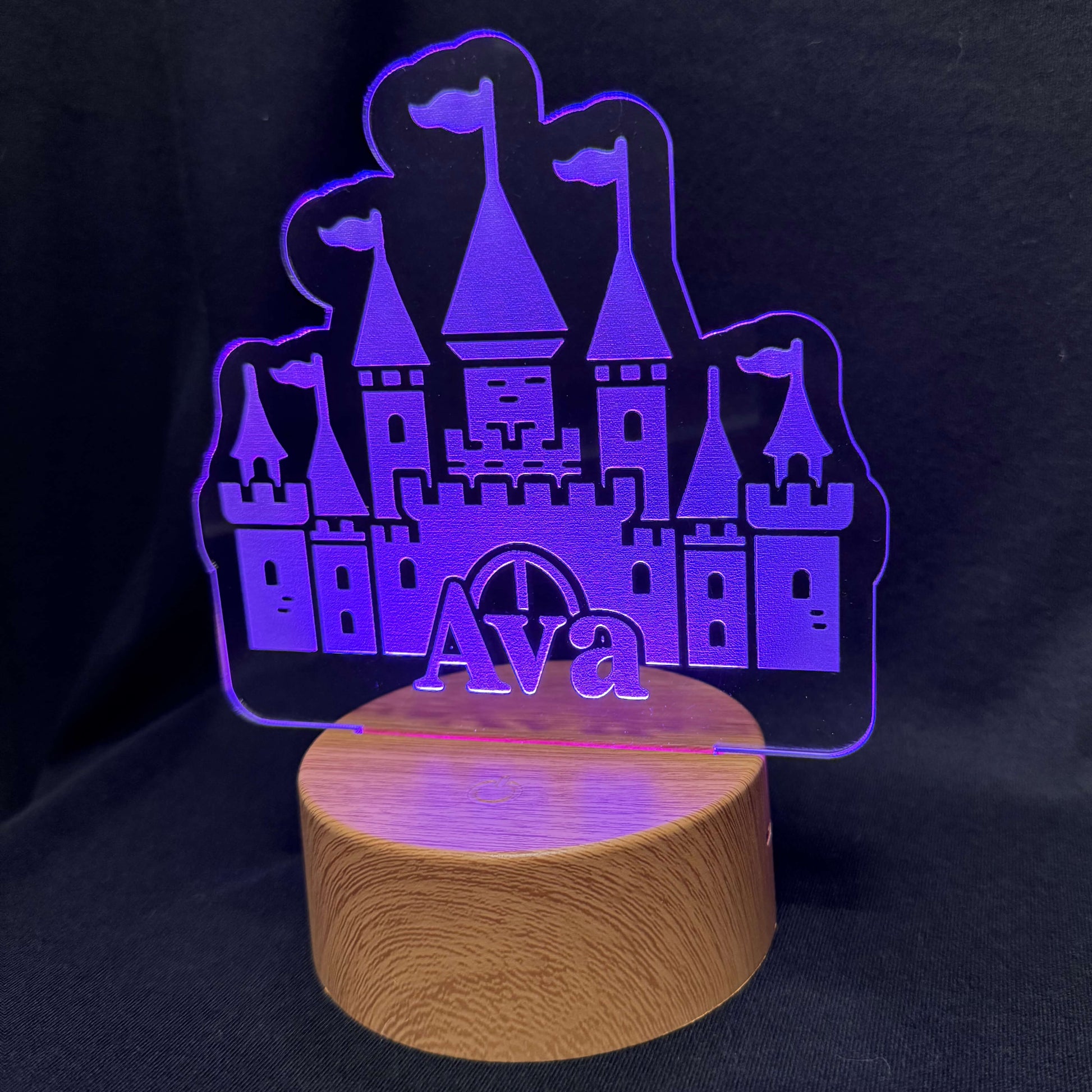 Purple castle-shaped LED lamp with 'Ava' on a wooden base against a black background