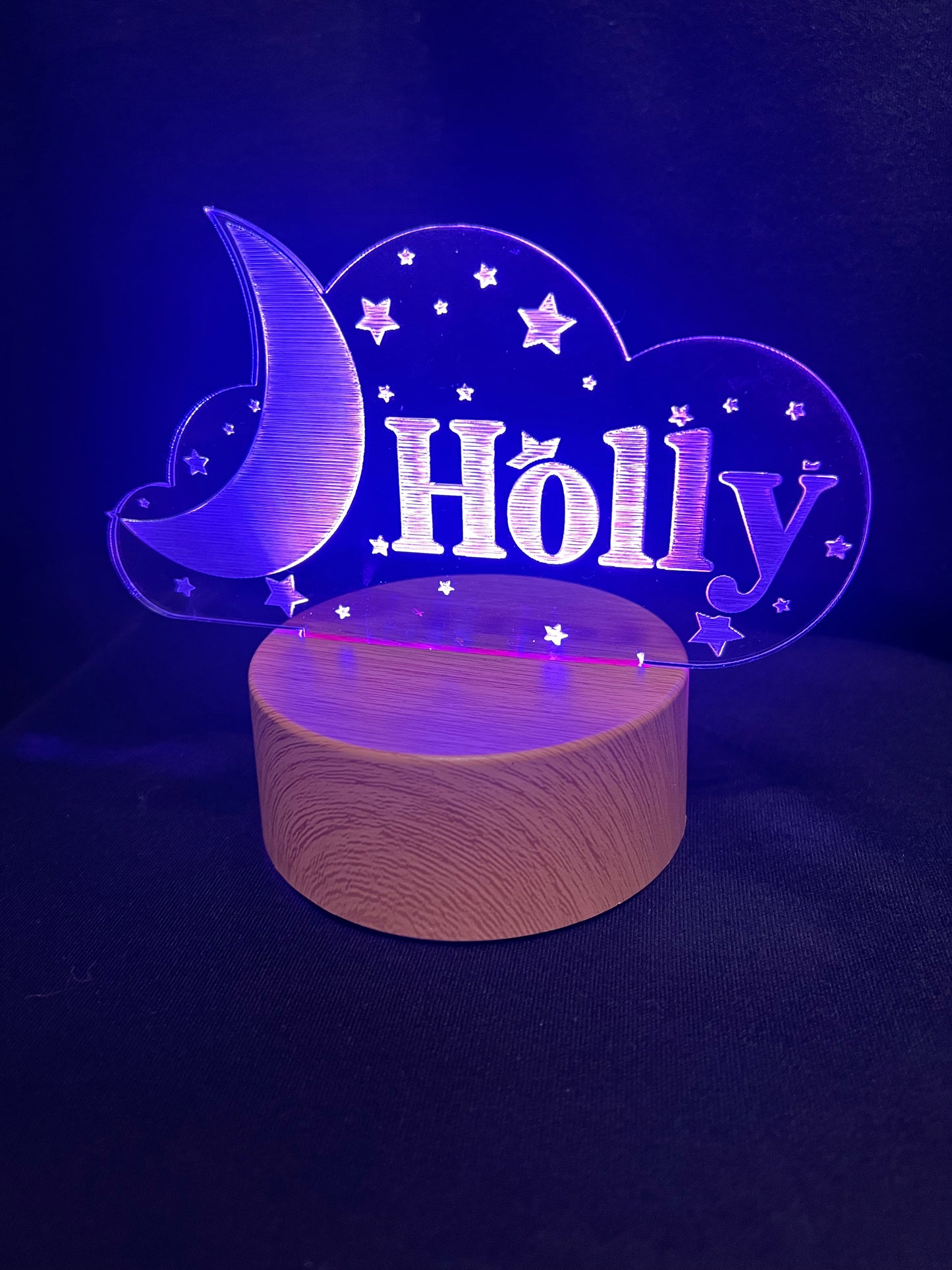 Custom acrylic LED night light with the name 'Holly' engraved in a cloud and moon design, glowing blue on a wooden-style base against a dark background
