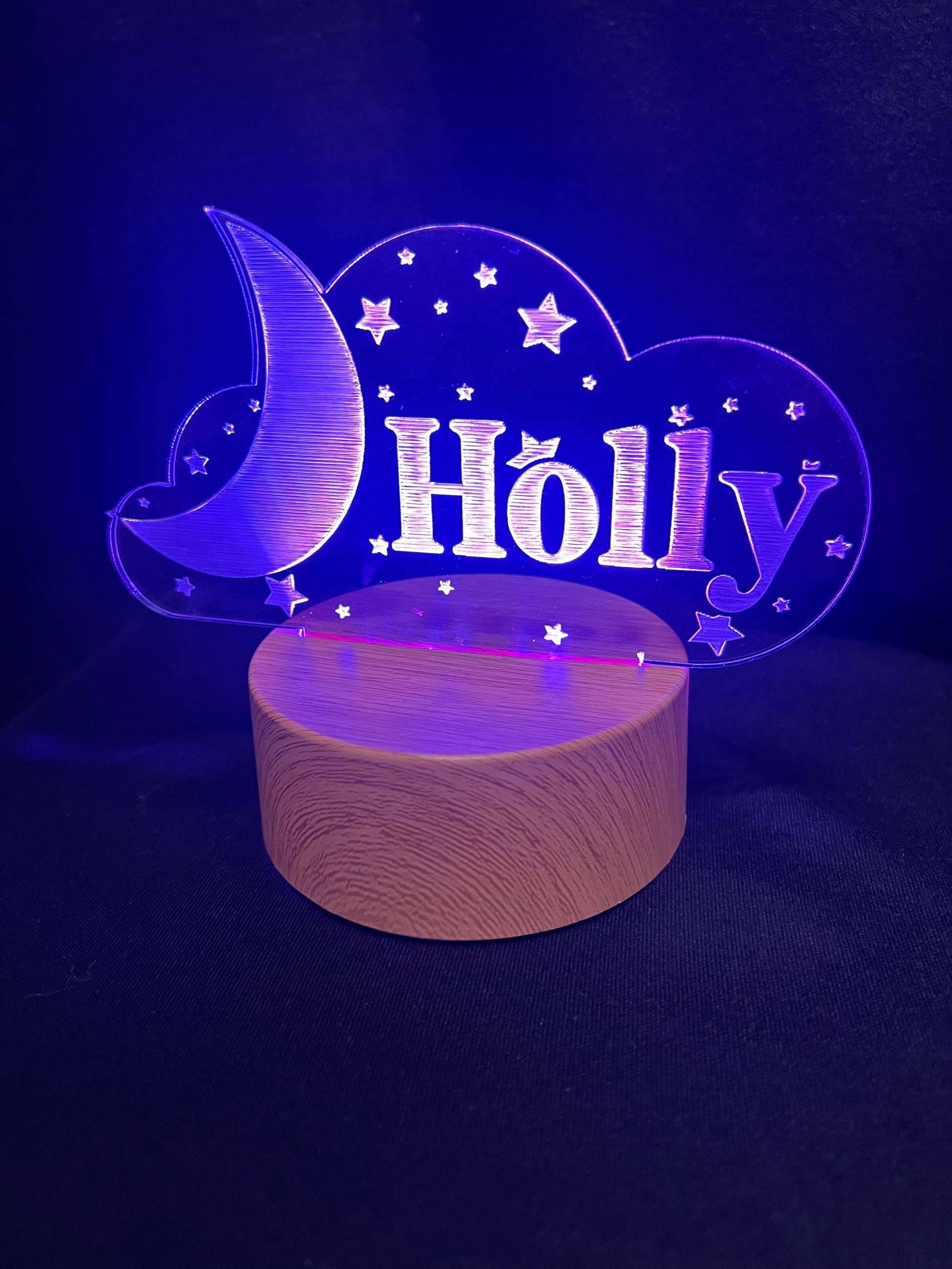 Custom acrylic LED night light with the name 'Holly' engraved in a cloud and moon design, glowing blue on a wooden-style base against a dark background