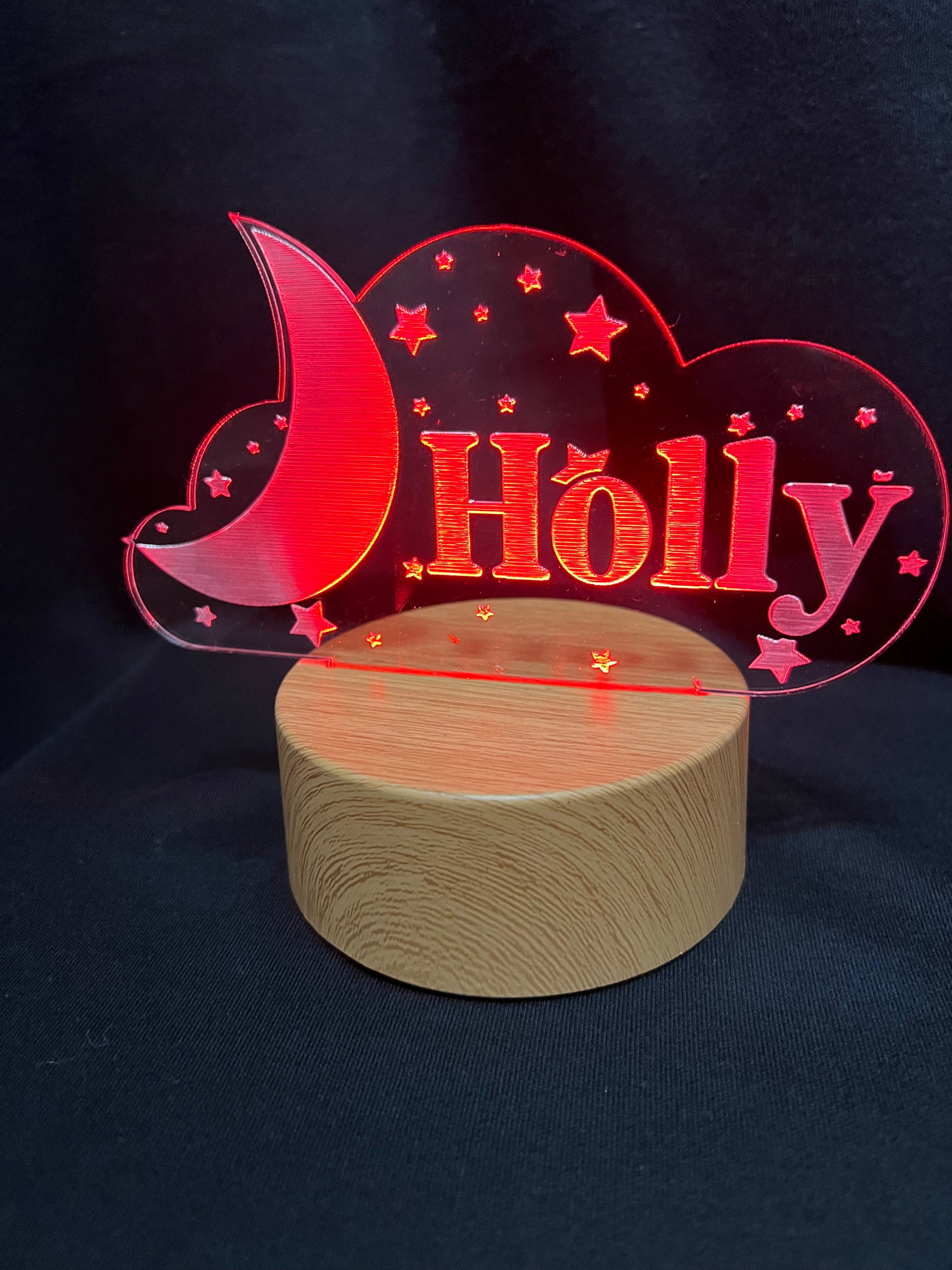 Custom acrylic LED night light with the name 'Holly' engraved in a cloud and moon design, glowing blue on a wooden-style base against a dark background