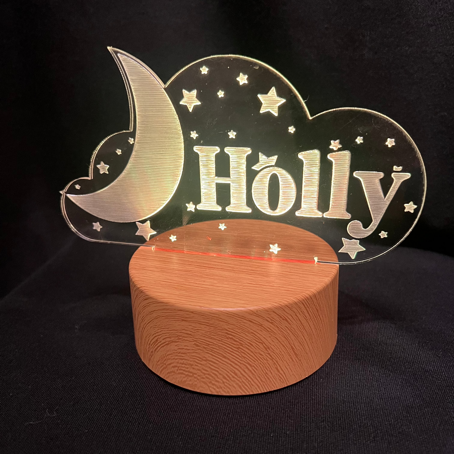 Custom acrylic LED night light with the name 'Holly' engraved in a cloud and moon design, glowing blue on a wooden-style base against a dark background