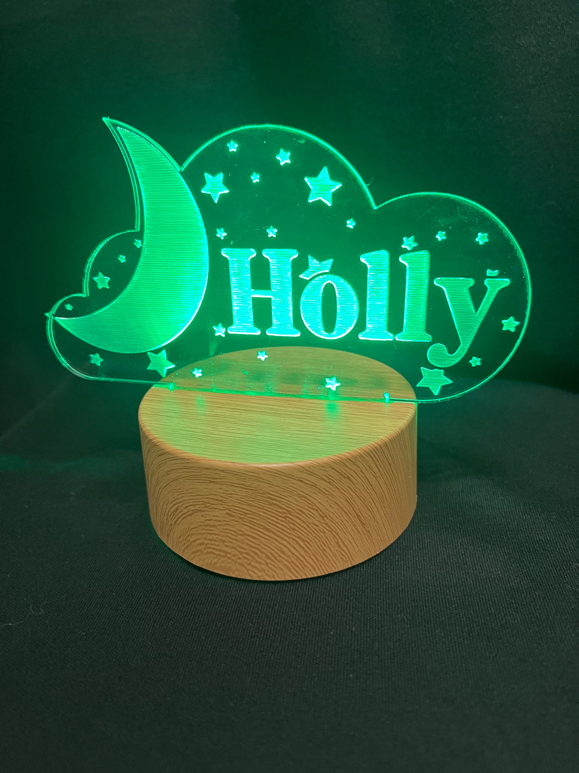 Custom acrylic LED night light with the name 'Holly' engraved in a cloud and moon design, glowing blue on a wooden-style base against a dark background
