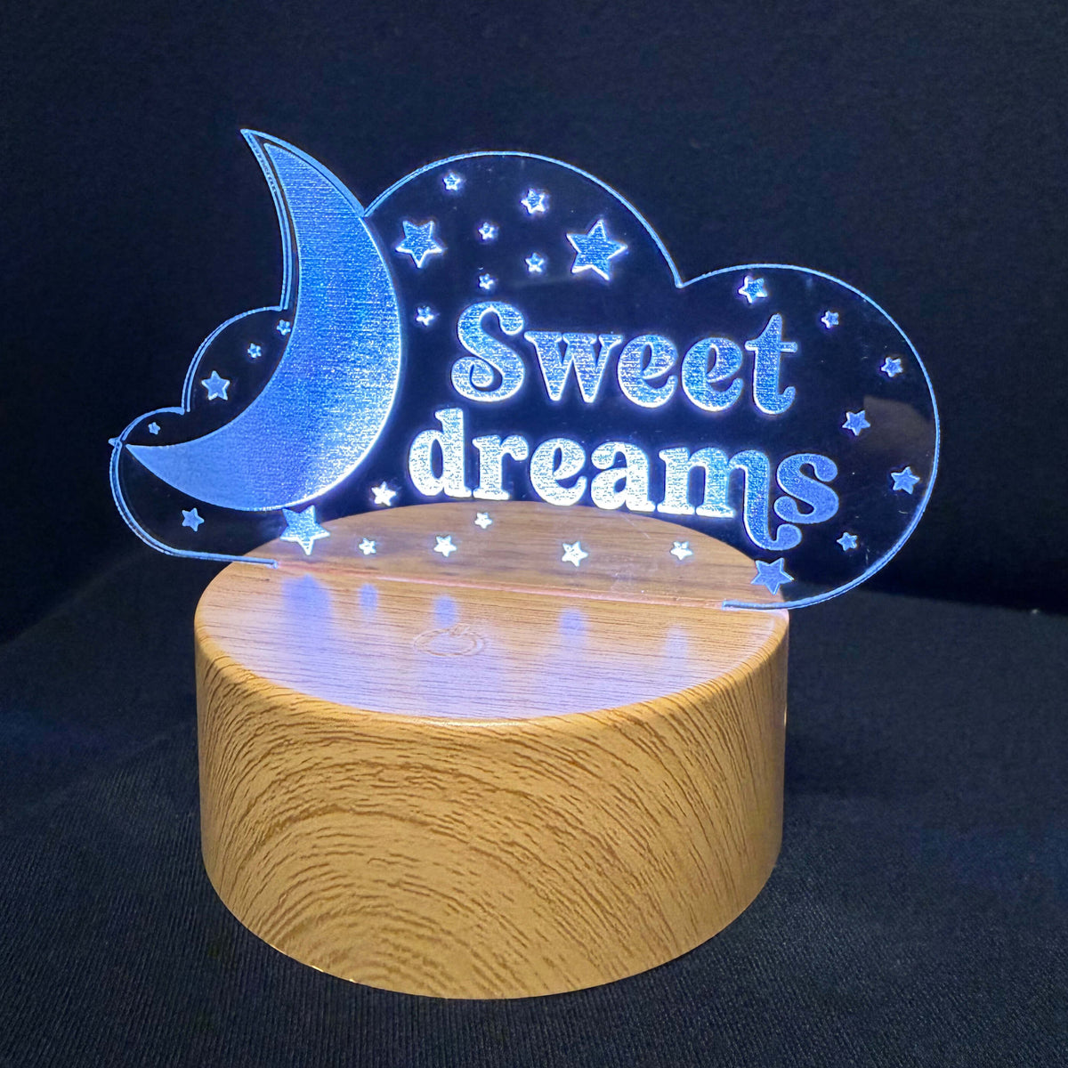A wooden night light lamp with a glowing blue acrylic cloud design that reads 'Sweet dreams' and includes a crescent moon and stars, set against a dark background.