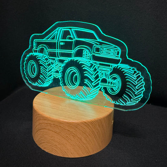 A 3D optical illusion night light featuring a glowing cyan monster truck outline on a round, light-colored wooden base, set against a dark black background.