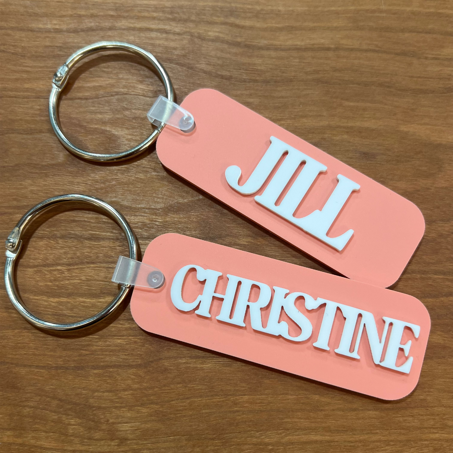 Two pink keychains with 'JILL' and 'CHRISTINE' text on a wooden surface