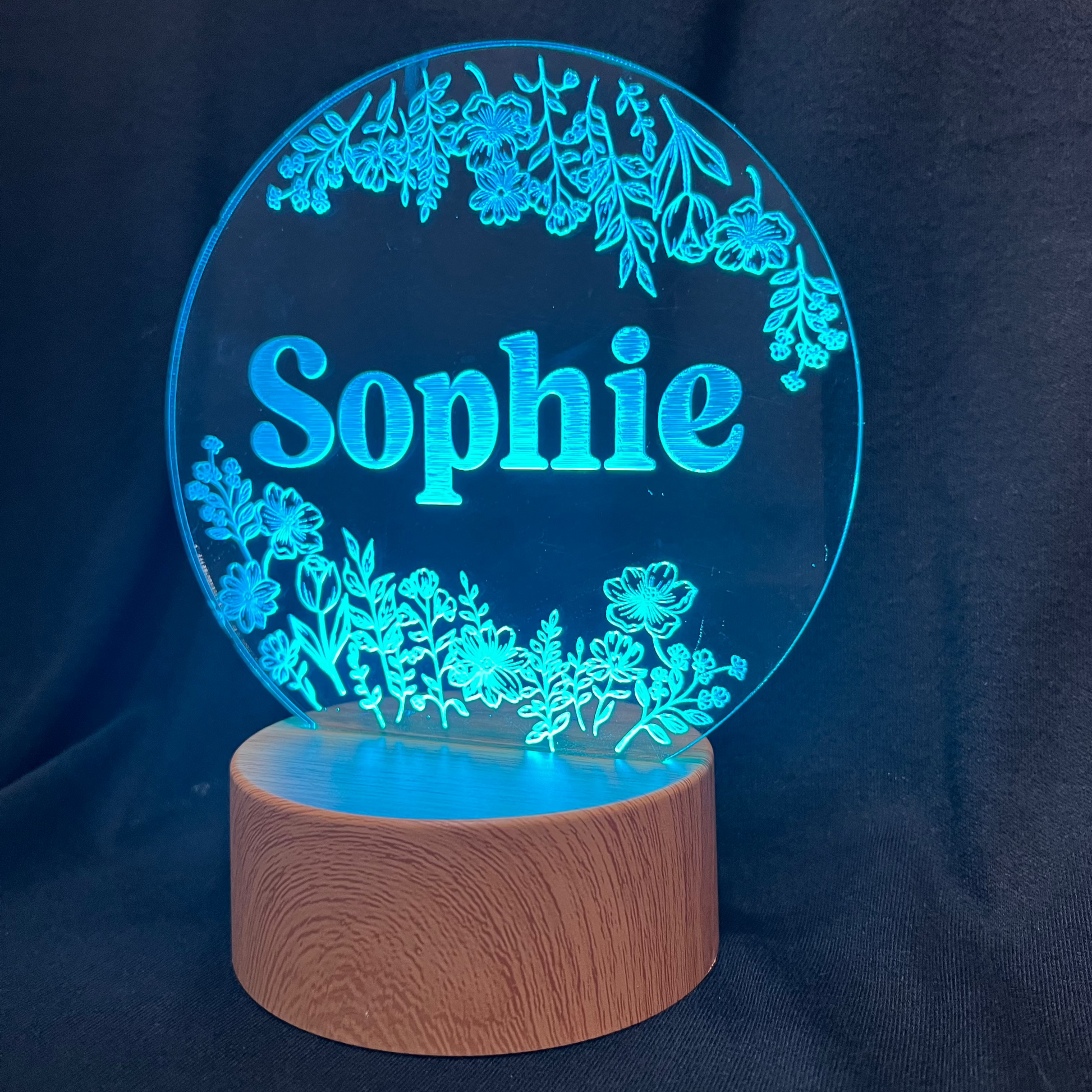 Personalized Wildflower Name Night Light featuring laser-engraved wildflowers surrounding a custom name on a clear acrylic panel, softly illuminated by an LED light on a wooden base
