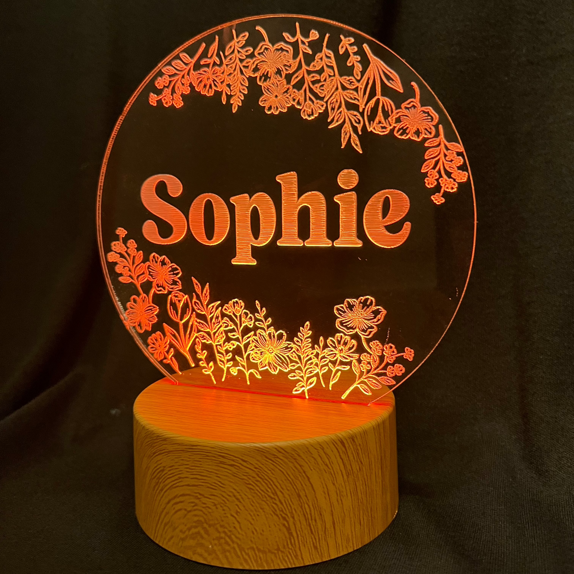 Personalized Wildflower Name Night Light featuring laser-engraved wildflowers surrounding a custom name on a clear acrylic panel, softly illuminated by an LED light on a wooden base